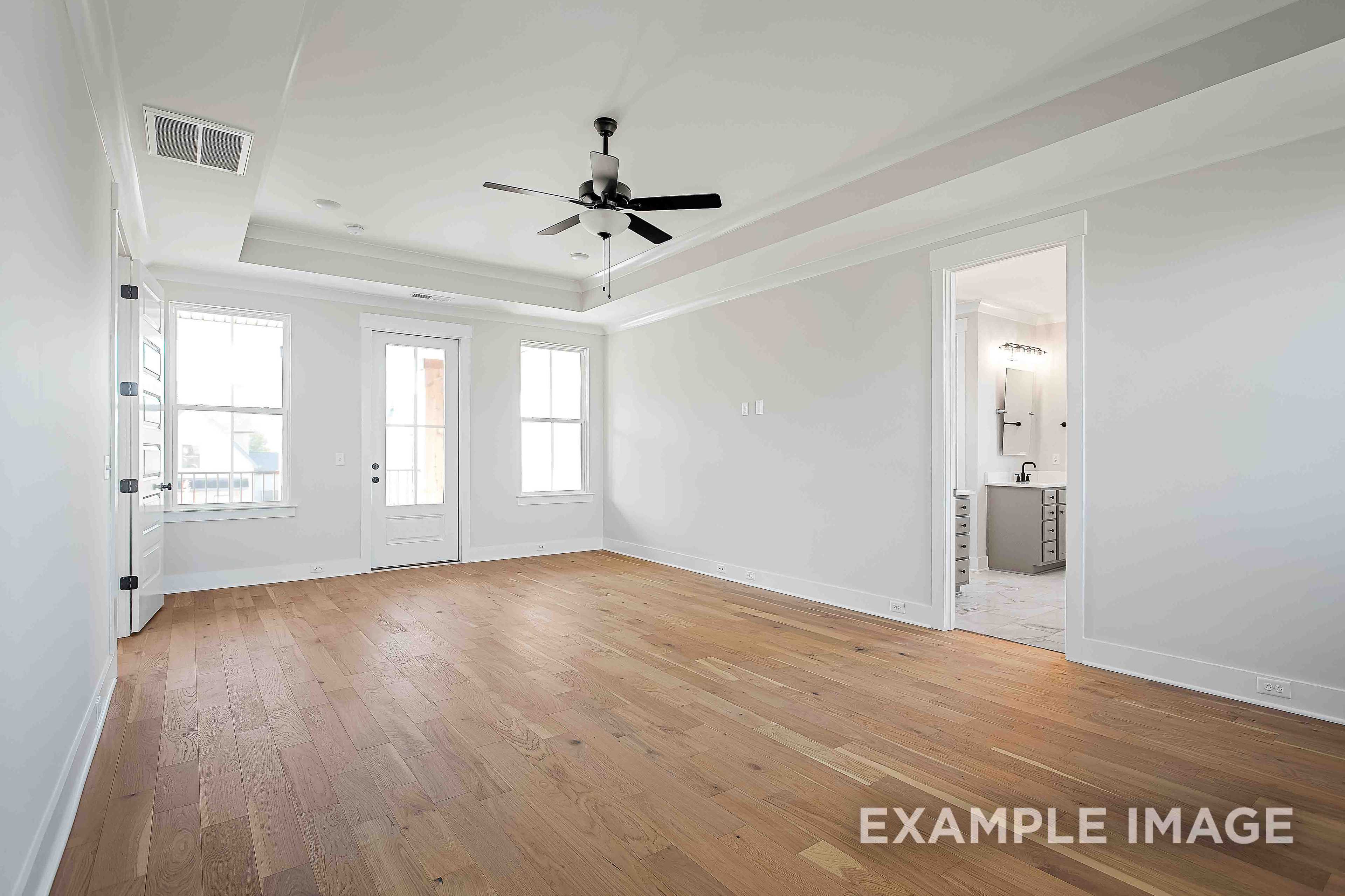 Spacious master bedroom in The Alston A featuring oak hardwood floors, ceiling fan, large windows, and en-suite bathroom