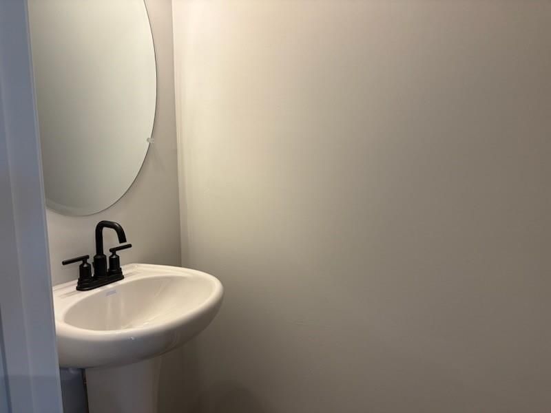 Modern powder room with white pedestal sink, black faucet, and round mirror in Davidson Homes Cary A, Winder, GA