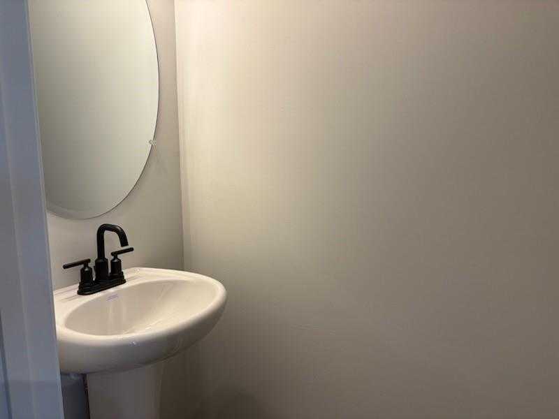 Modern powder room with white pedestal sink, black faucet, and round mirror in Davidson Homes Cary A, Winder, GA