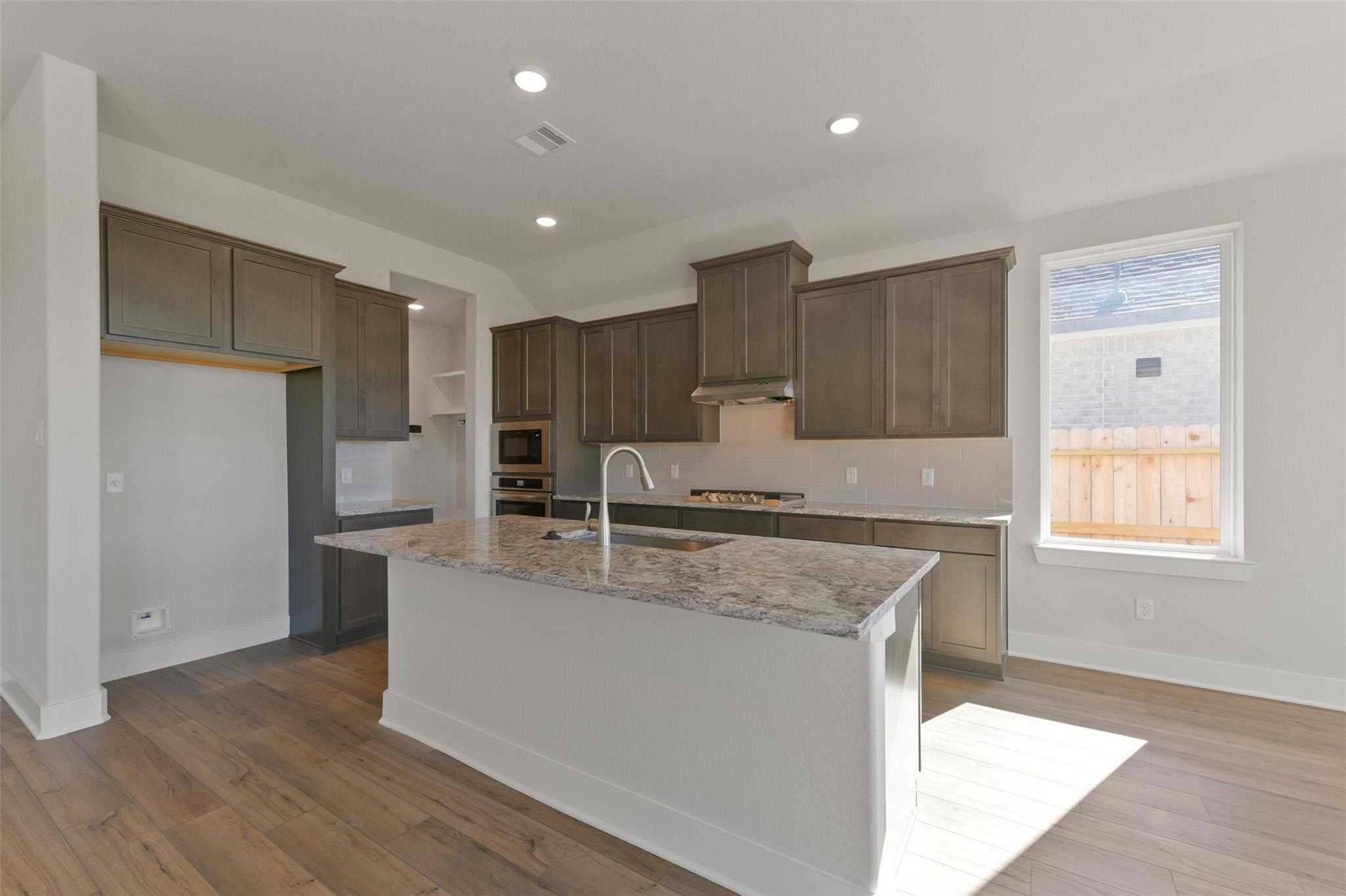Modern kitchen with taupe shaker cabinets, granite island, stainless appliances in Davidson Homes The Diana A, Lago Mar, Texas City