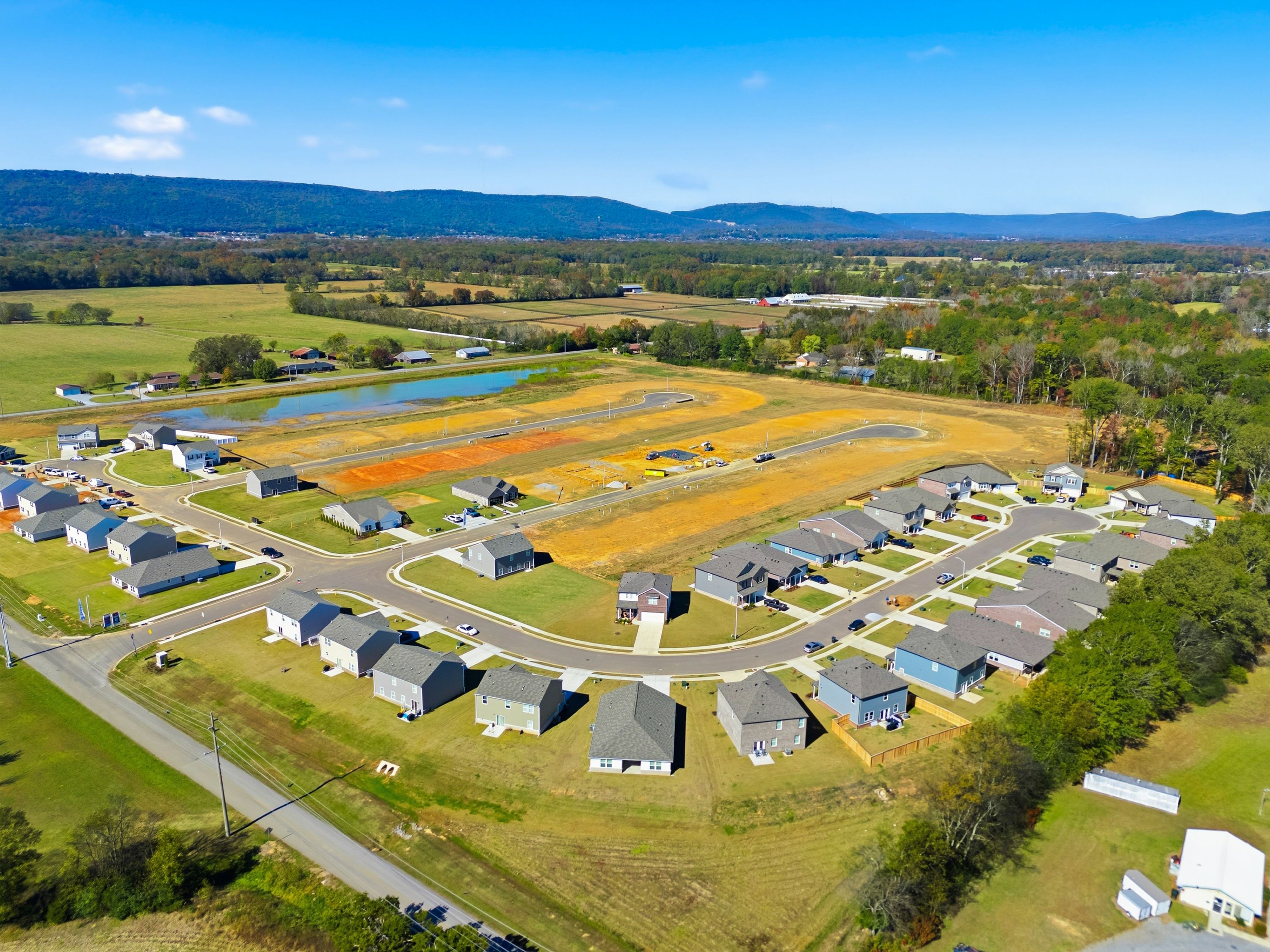 Aerial view of Ramsay Cove neighborhood in Owens Cross Roads AL with new homes, construction sites, pond, fields, and mountain backdrop