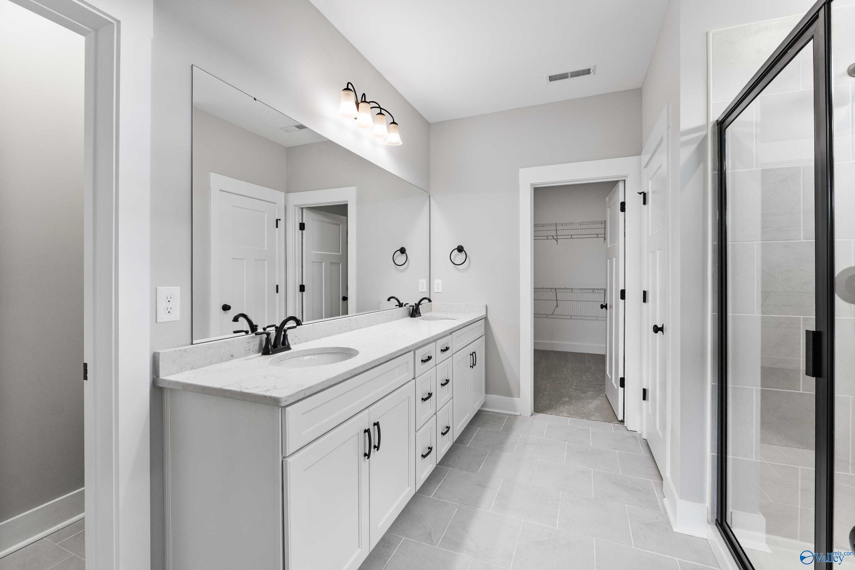 Elegant master bathroom with double vanity, large mirror, walk-in closet, and glass shower in Davidson Homes The Arcadia, Huntsville, Alabama