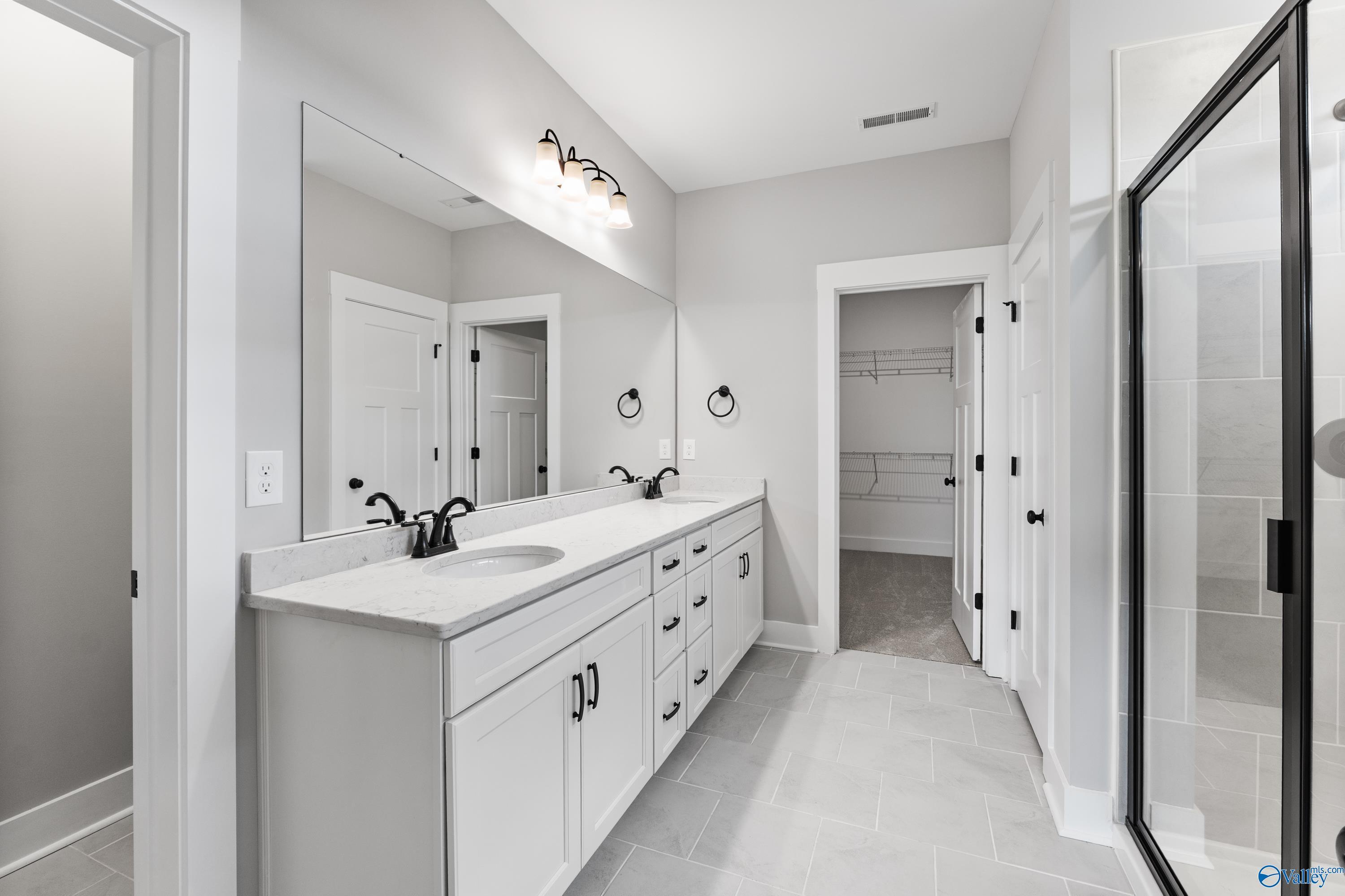 Elegant master bathroom with double vanity, large mirror, walk-in closet, and glass shower in Davidson Homes The Arcadia, Huntsville, Alabama