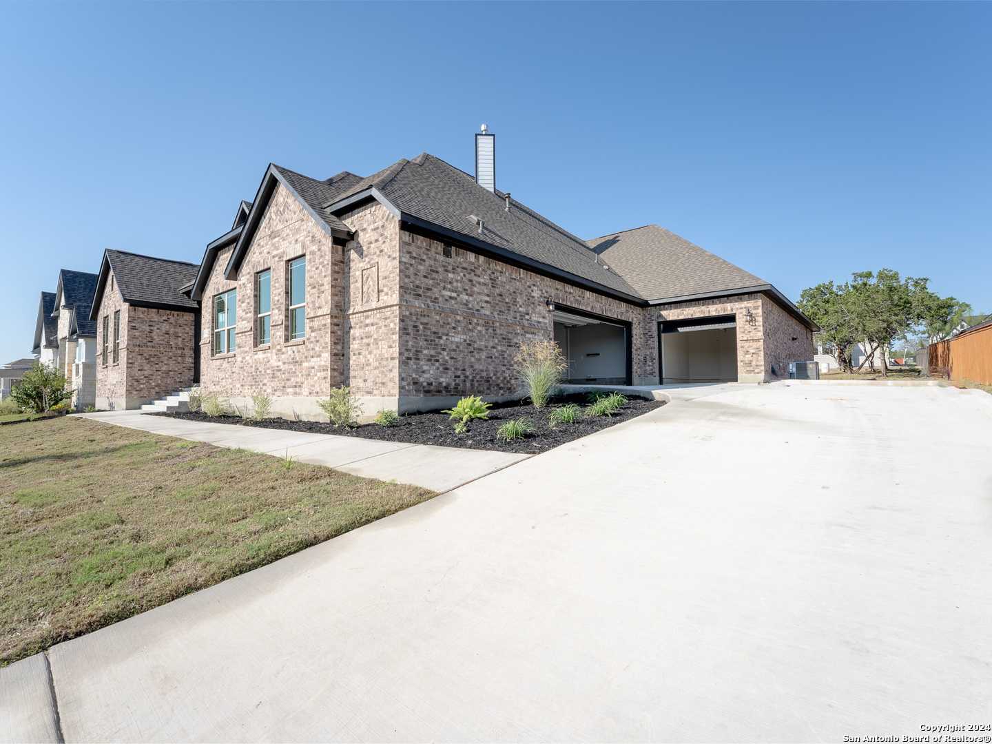 Modern brick 1-story home with 2-car garage, driveway, and landscaping in Potranco Oaks, Castroville, Texas