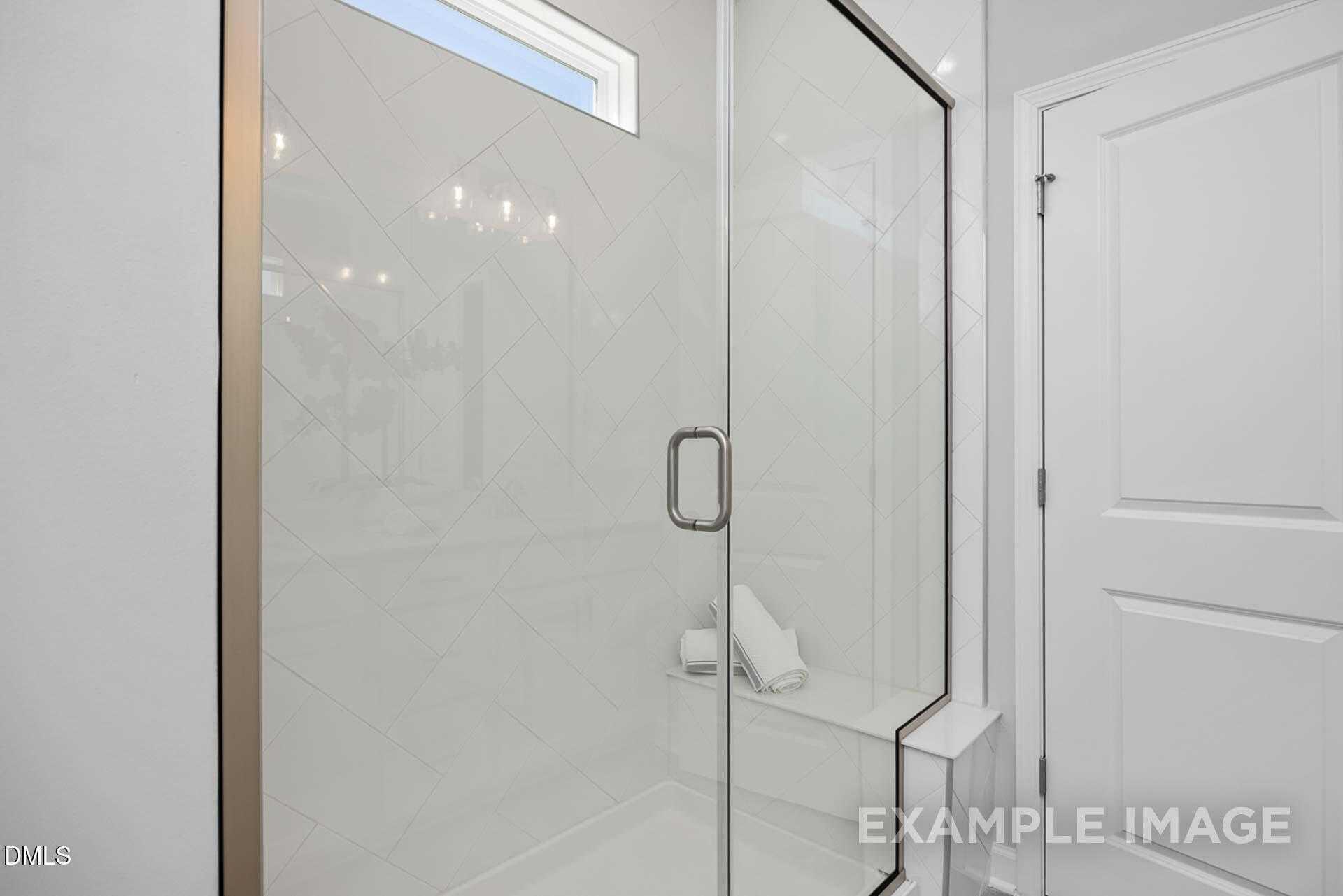 Frameless glass shower with white subway tiles, built-in bench, and towels in master bath of 3-bedroom The Carter C home in Lillington, NC