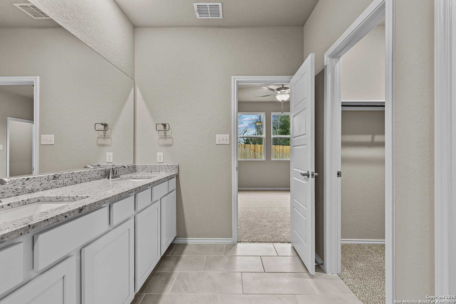 Modern master bathroom with double marble vanity, large mirrors, and walk-in closet door in Davidson Homes The Douglas F, San Antonio