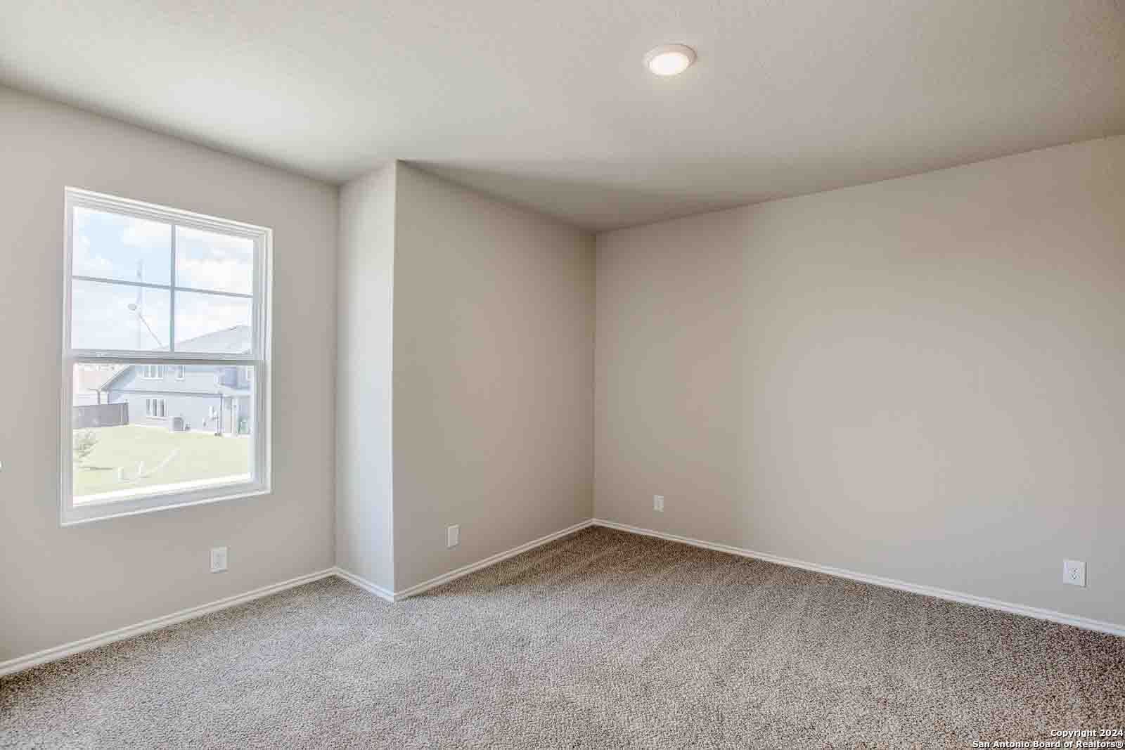 Empty bedroom with neutral beige walls, plush carpet, recessed lighting, and large window overlooking lawn in Davidson Homes The Murray H, Seguin, Texas