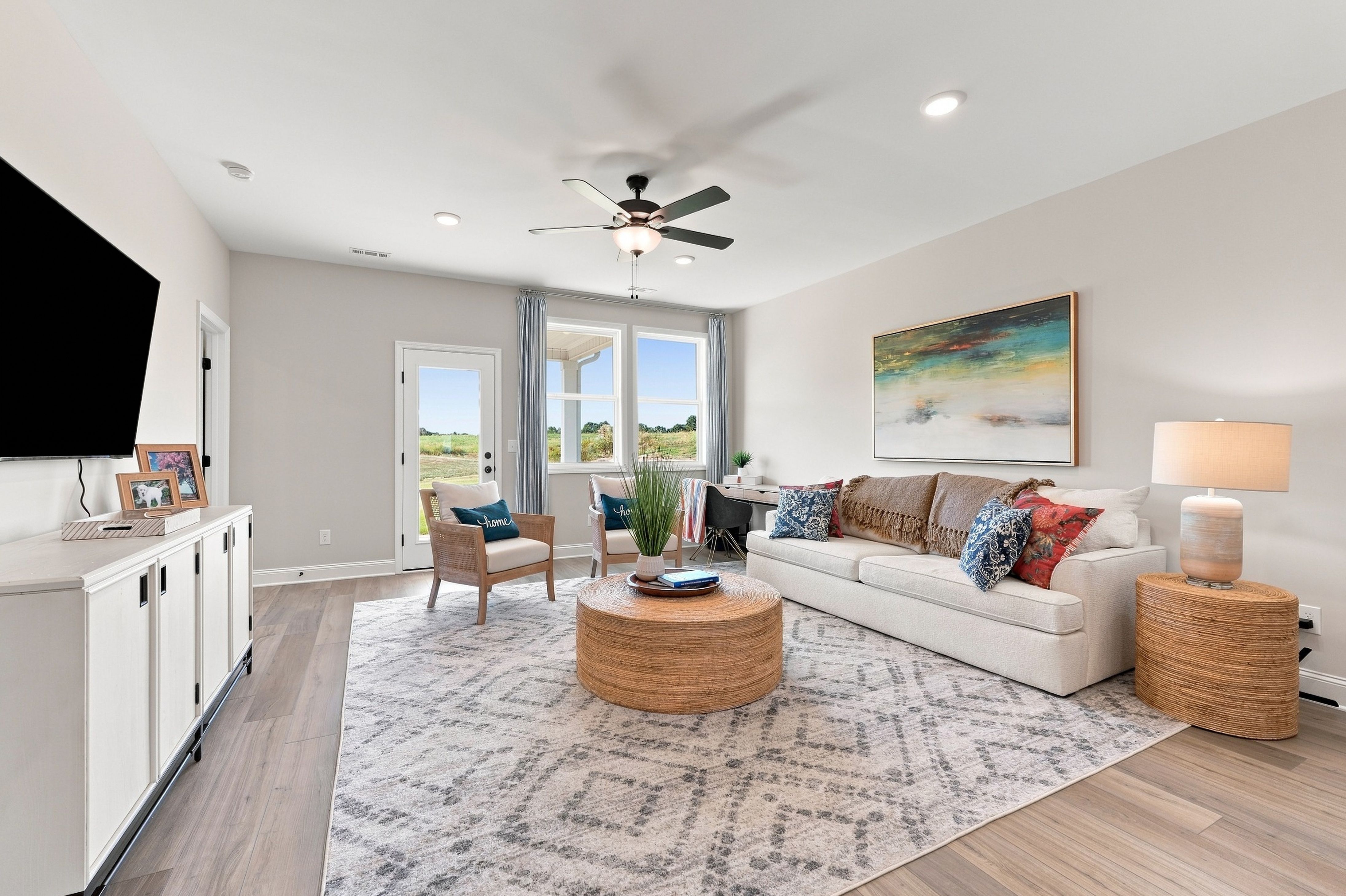 Bright living room at Bailey Park in Fayetteville, Tennessee by Davidson Homes with white sofa, rattan ottoman, and ceiling fan