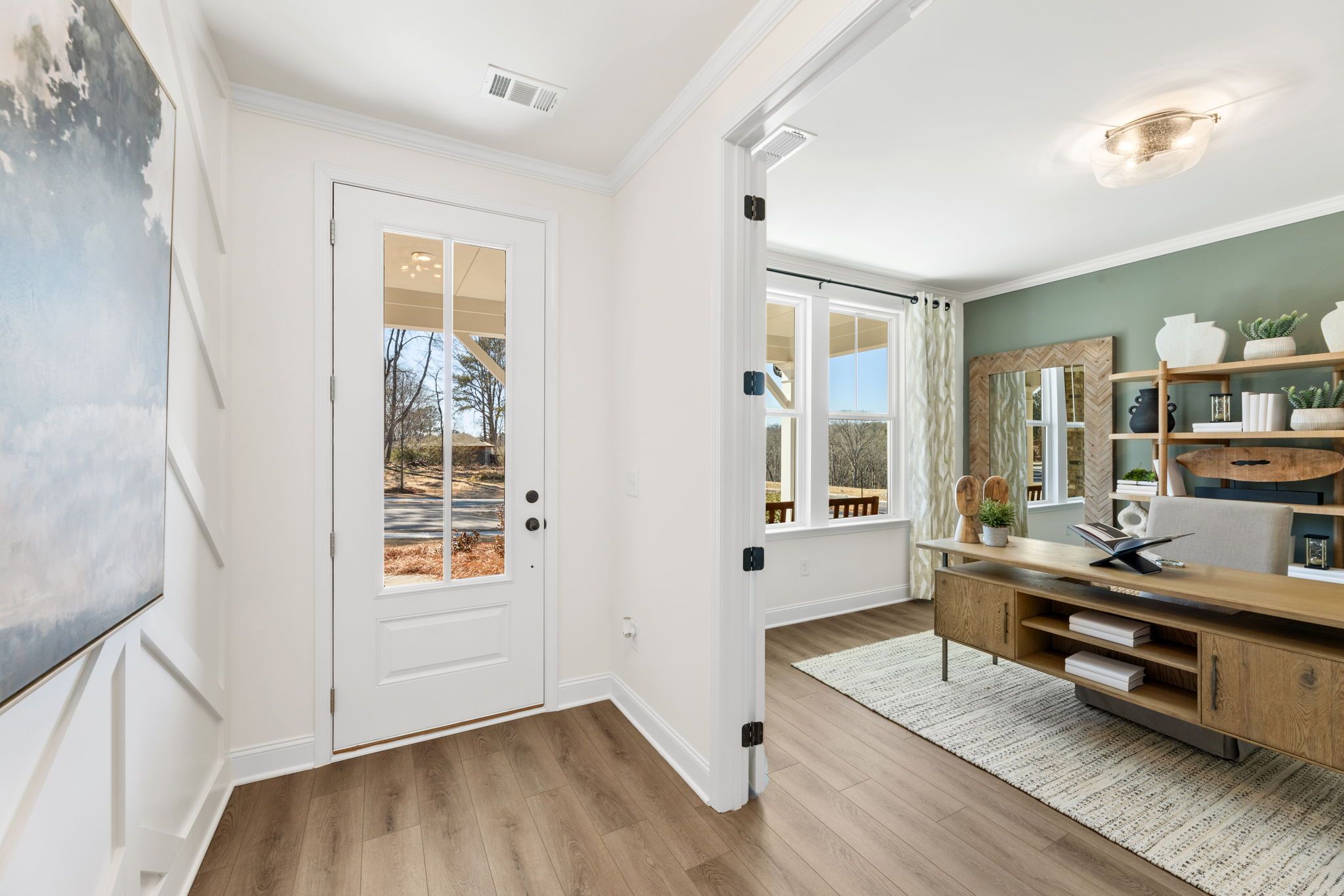 Spacious home office in Fern Hollow Buford GA with wooden desk, built-in bookshelves, plants, and glass door to wooded view