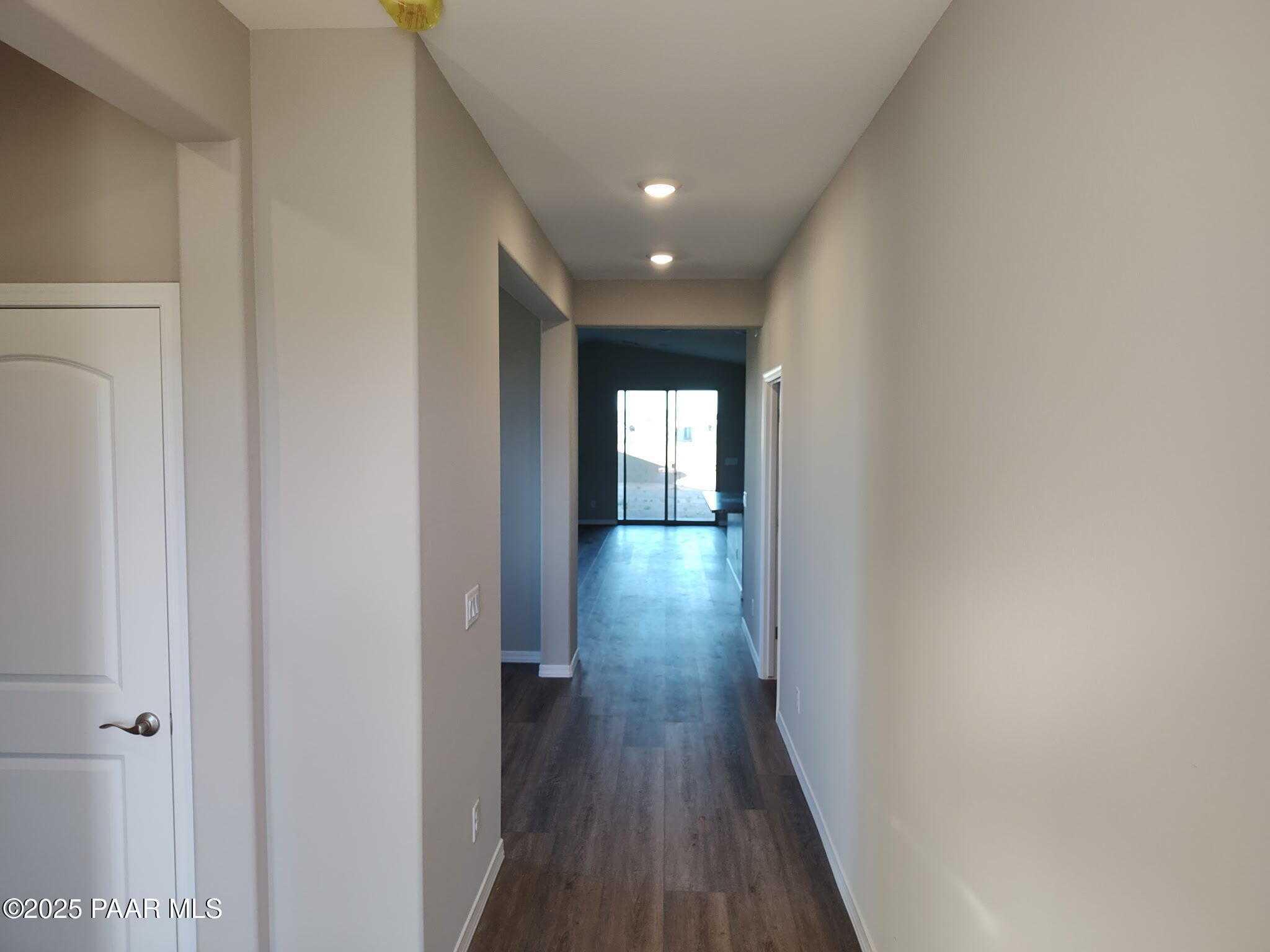 Long hallway with hardwood floors, beige walls, and recessed lights leading to sliding glass doors in Davidson Homes The Frontier A, Prescott Valley, Arizona