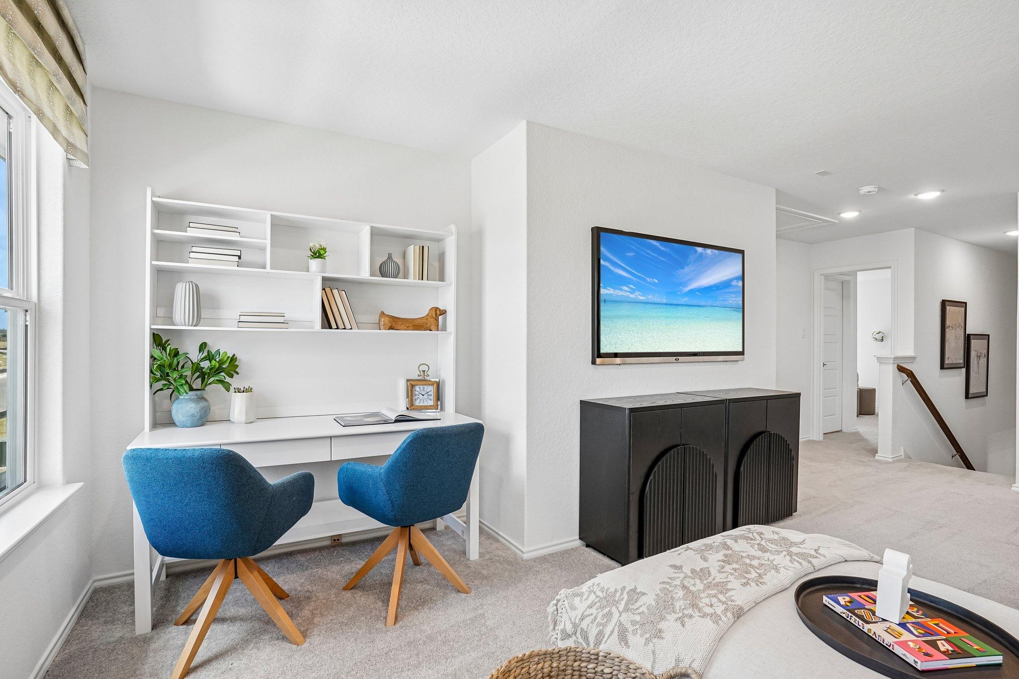 Home office space at Morgan Meadows in San Antonio with white desk, blue chairs, and wall-mounted TV by Davidson Homes.