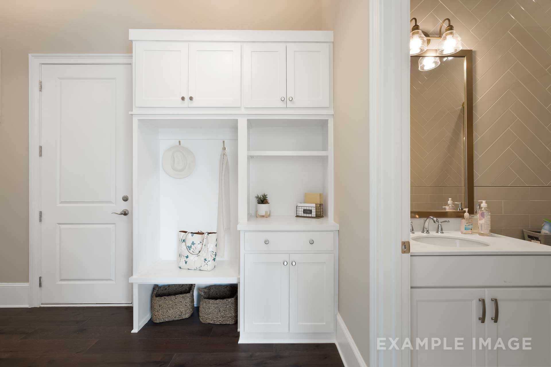Spacious mudroom in The Seaside B with white cabinetry, built-in bench, hooks, sink, and herringbone wall, Davidson Homes Woodstock GA