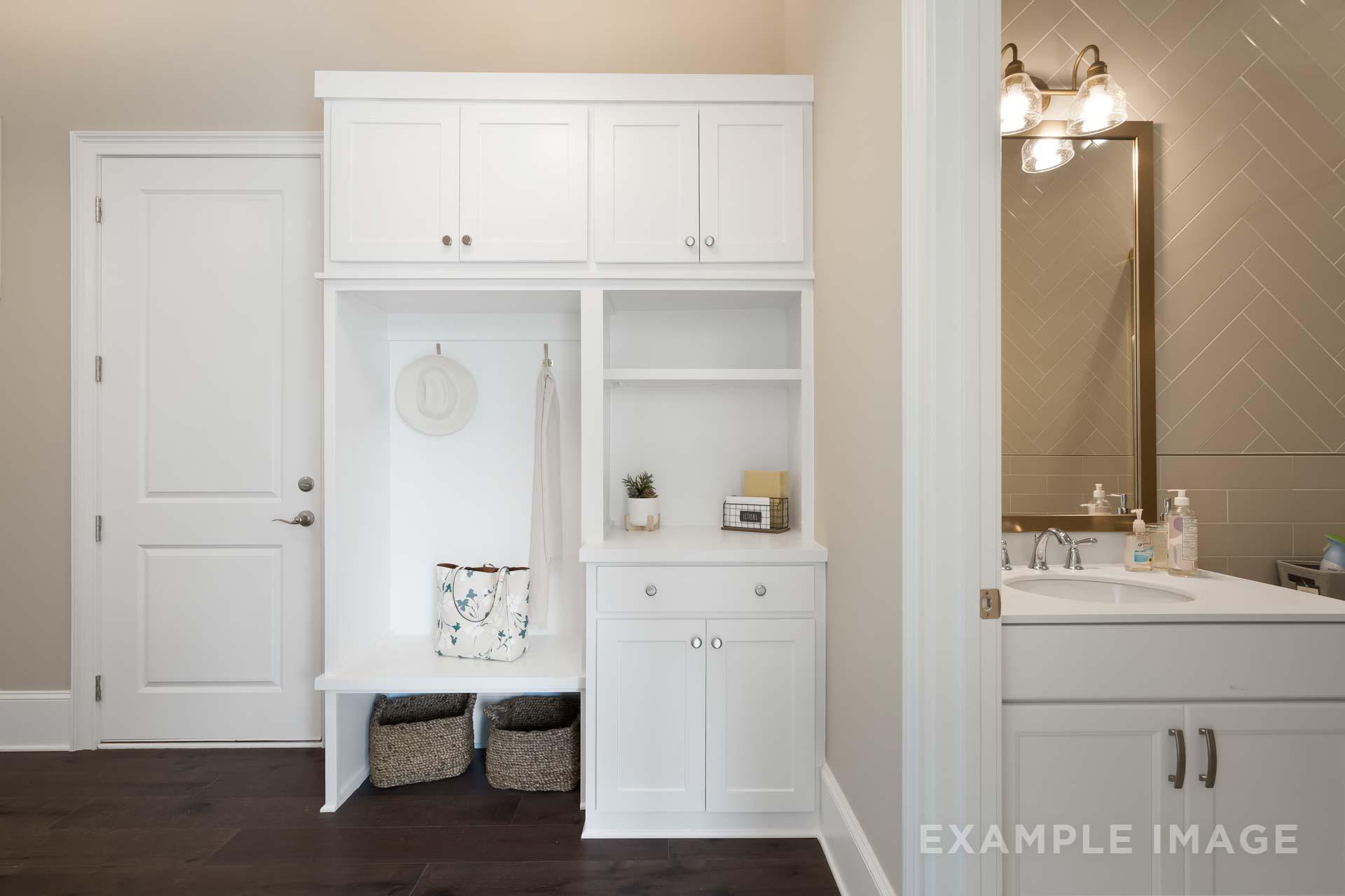 Spacious mudroom in The Seaside C featuring white cabinetry, coat hooks, storage baskets, and adjacent powder room vanity