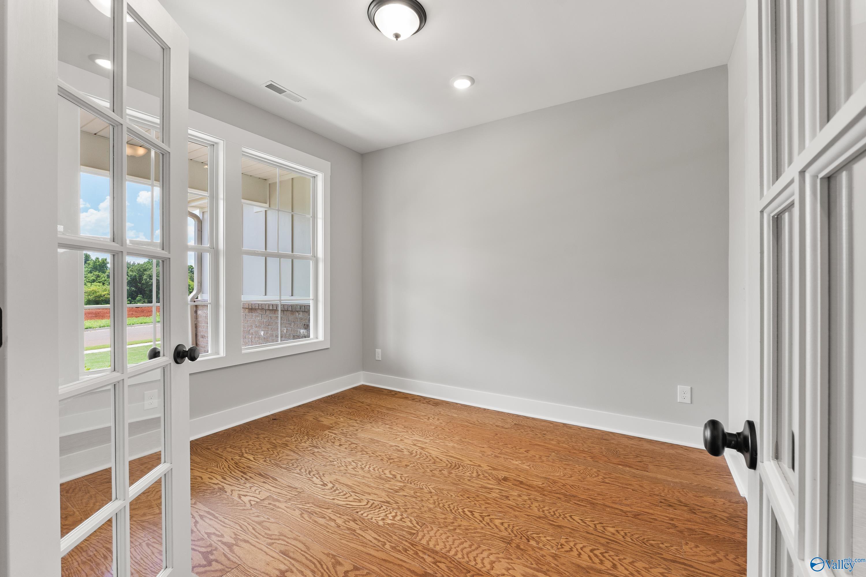Bright empty study with light gray walls, oak hardwood floors, French doors, and large windows in Davidson Homes The Arcadia, Huntsville AL