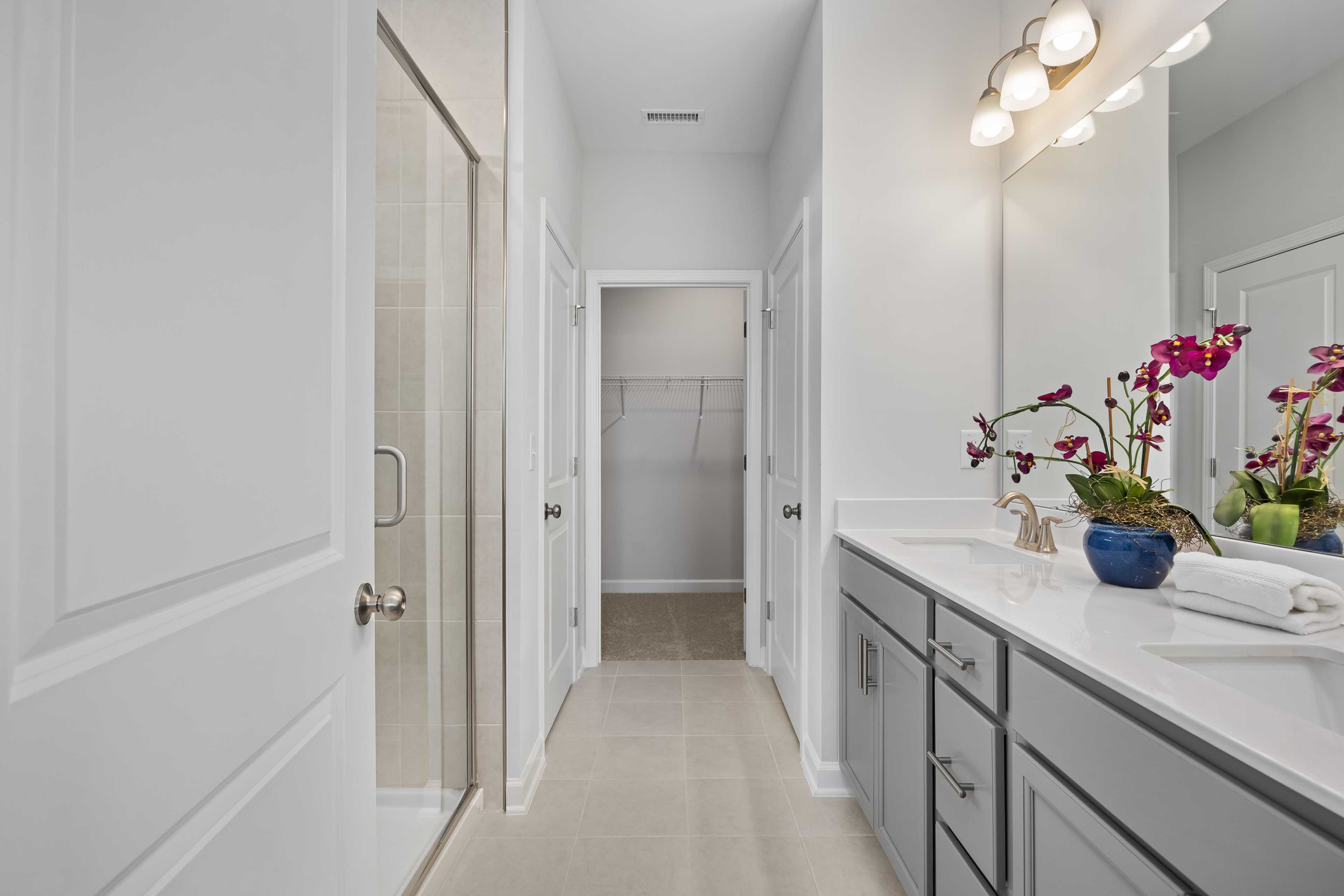 Spacious primary bathroom at Woodland Crossing in Zebulon NC with glass shower, double vanity, orchids and walk-in closet