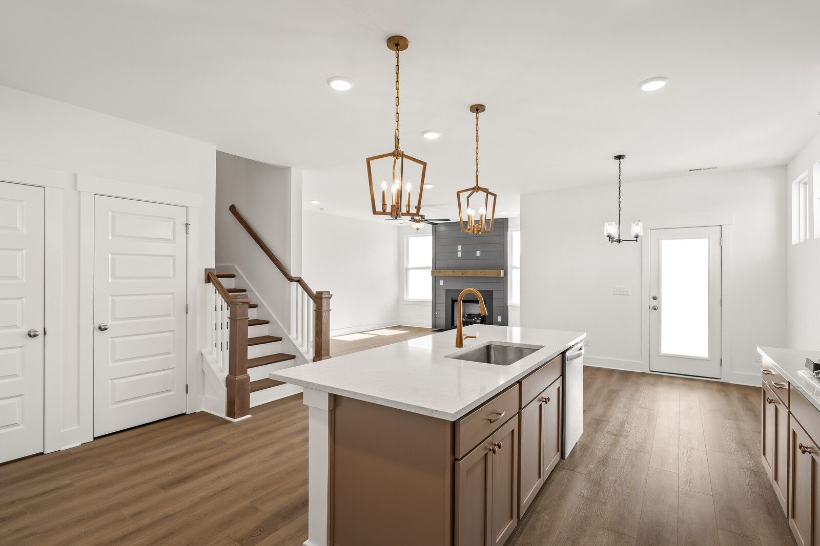 Open-concept kitchen with white quartz island, brown cabinets, gas fireplace, hardwood floors, and staircase in Davidson Homes The Ash A, Gallatin, TN