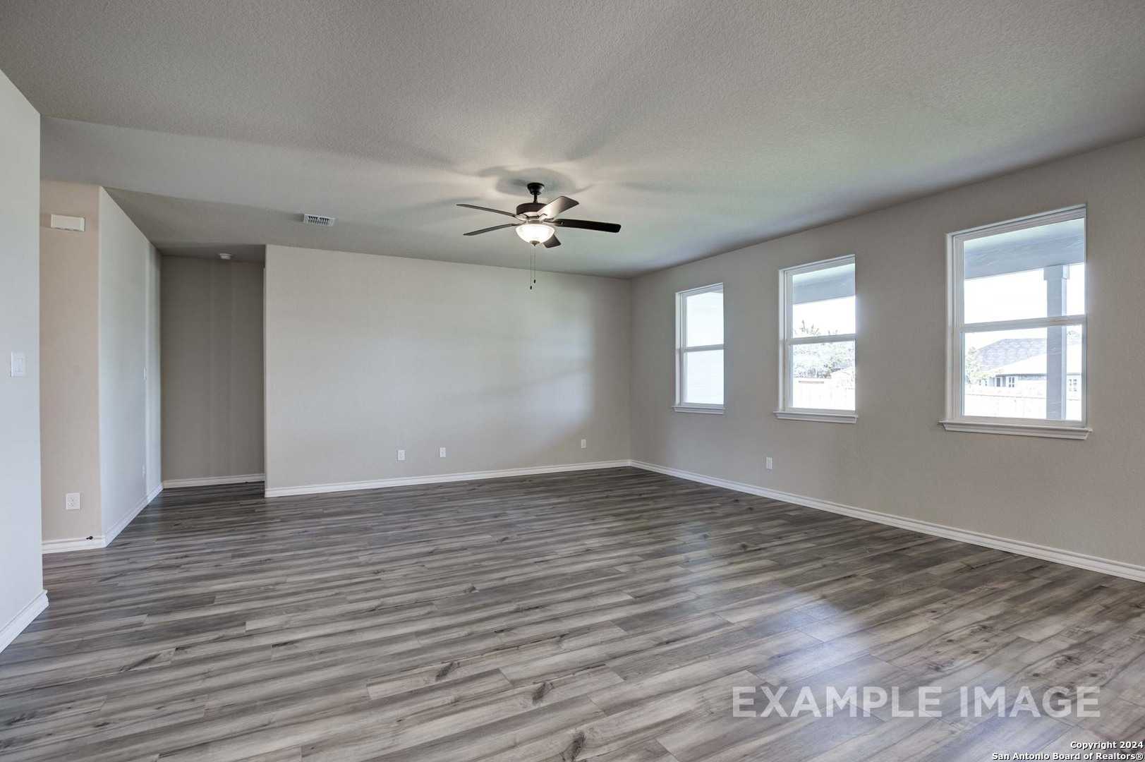 Spacious living room with ceiling fan, large windows, and gray hardwood floors in Davidson Homes The Rockford G, Ladera, San Antonio
