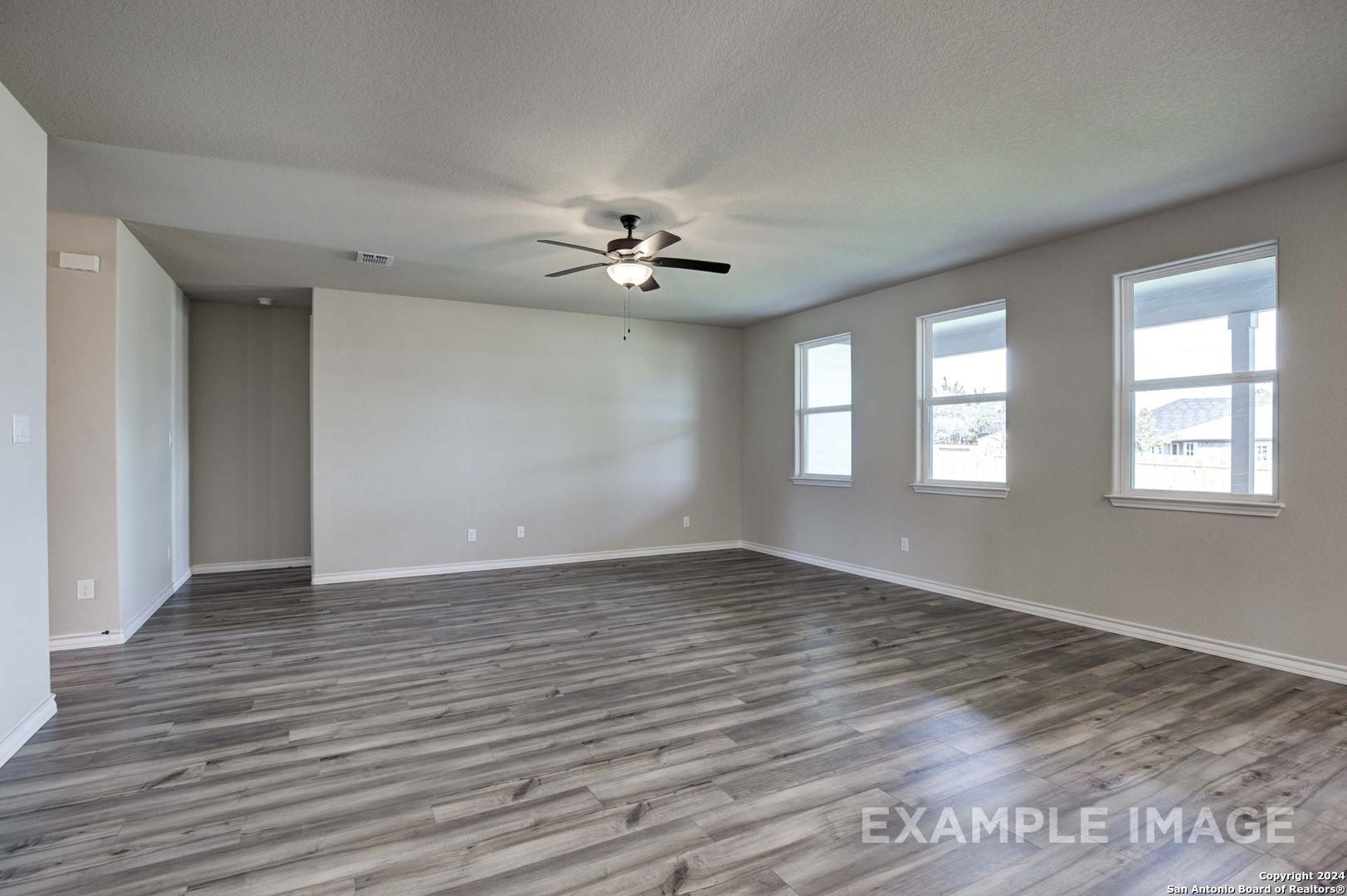 Spacious living room with ceiling fan, large windows, and gray hardwood floors in Davidson Homes The Rockford G, Ladera, San Antonio