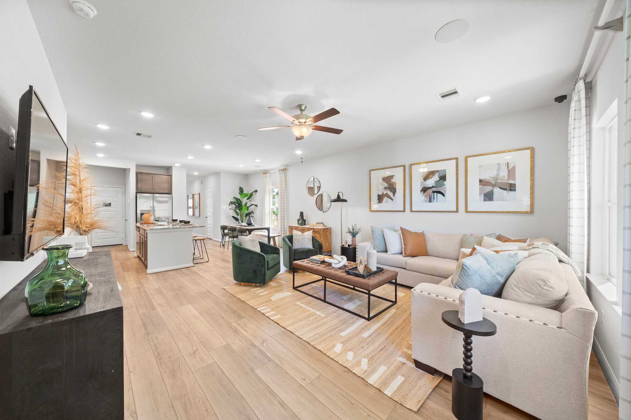 Open-concept living room and kitchen at Caney Creek Place in Conroe Texas with hardwood floors, sectional sofa, and ceiling fan