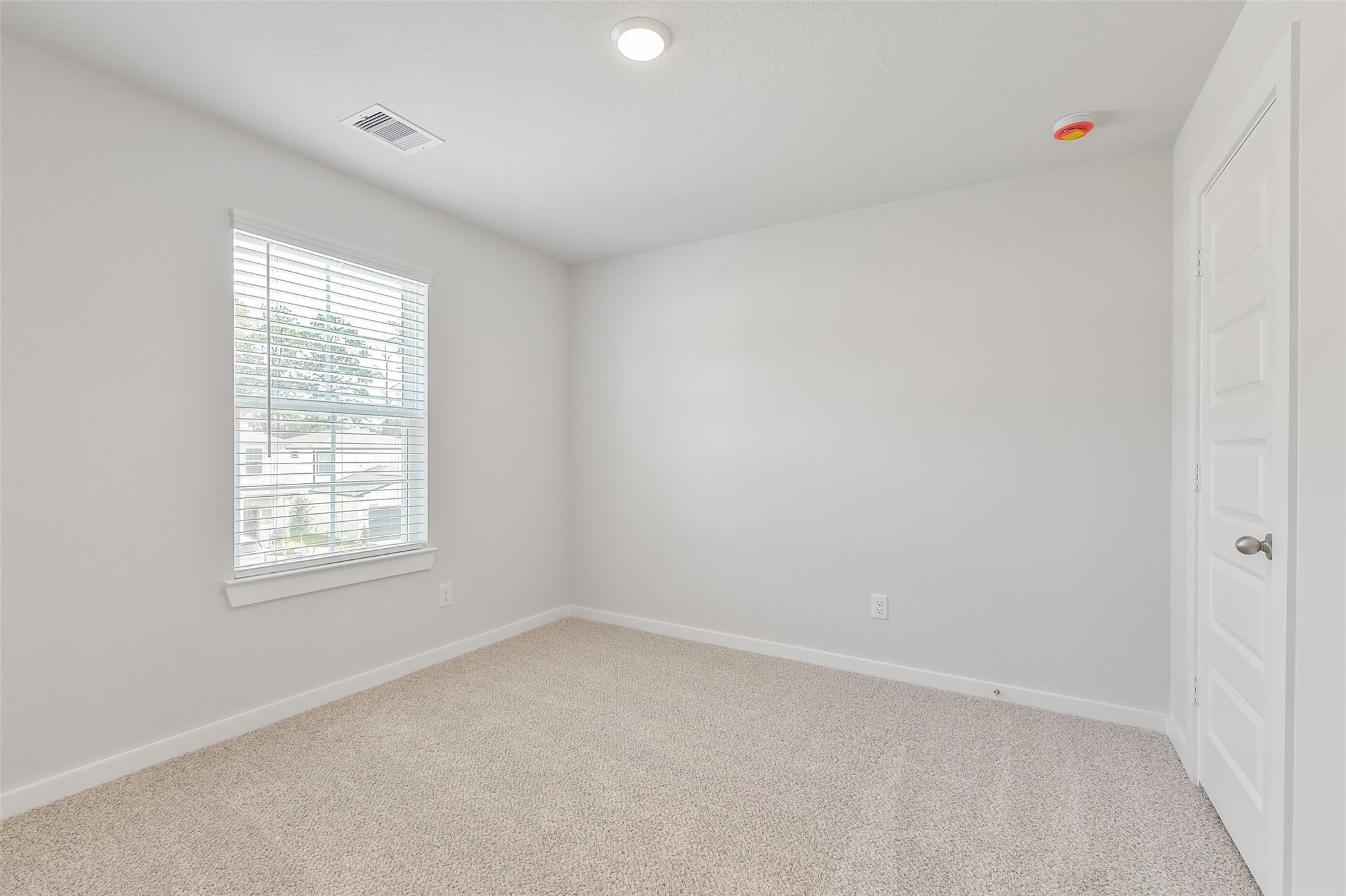 Bright secondary bedroom with light gray walls, beige carpet, and window blinds in Davidson Homes The Trinity F, Magnolia, Texas