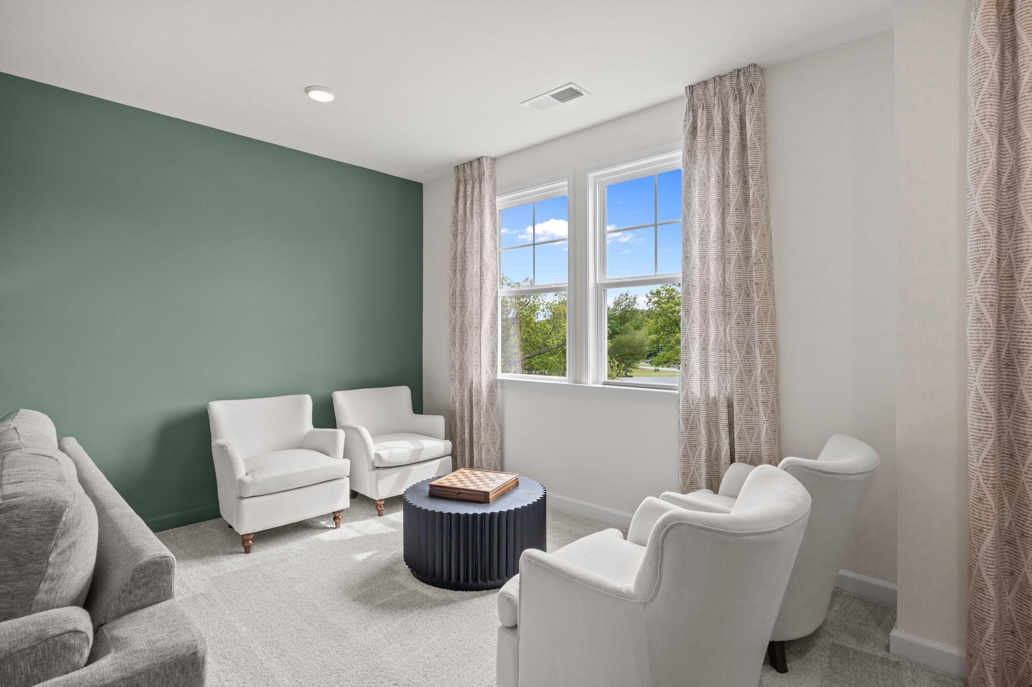 Cozy sitting area at Springvale South in Fuquay-Varina with white armchairs, green accent wall, and patterned curtains.