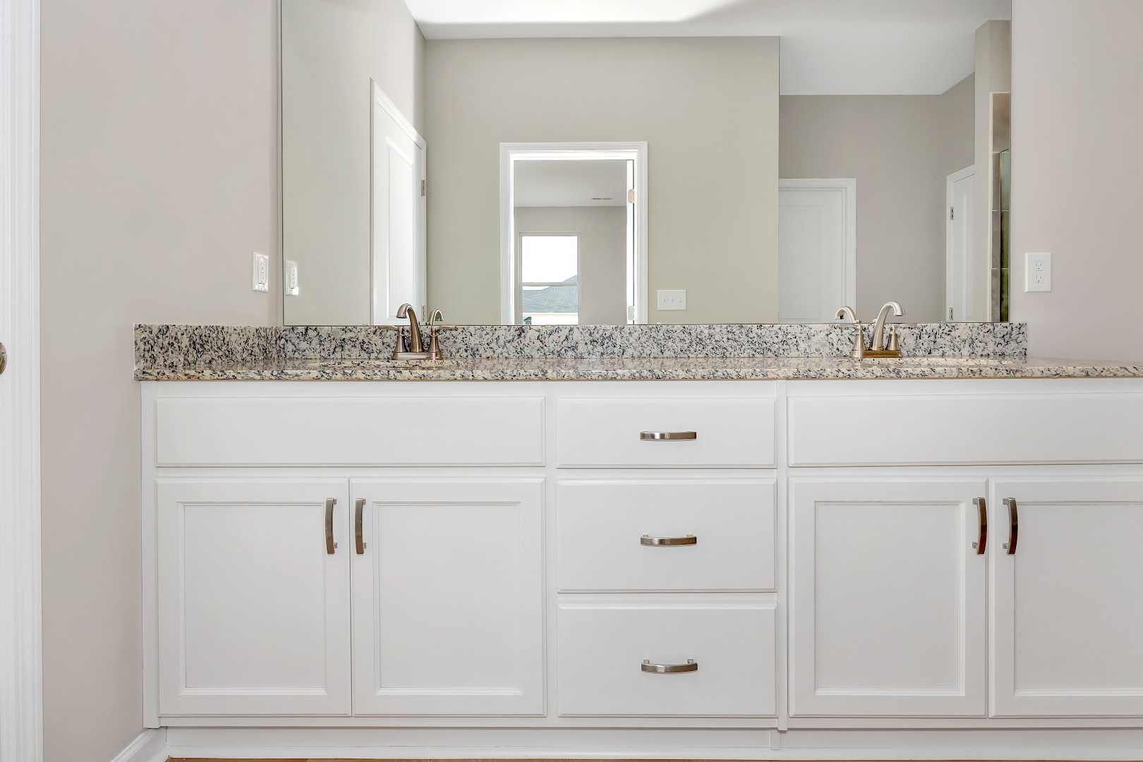 Master bathroom double vanity in The Orion home with white shaker cabinets, granite countertop, and dual sinks