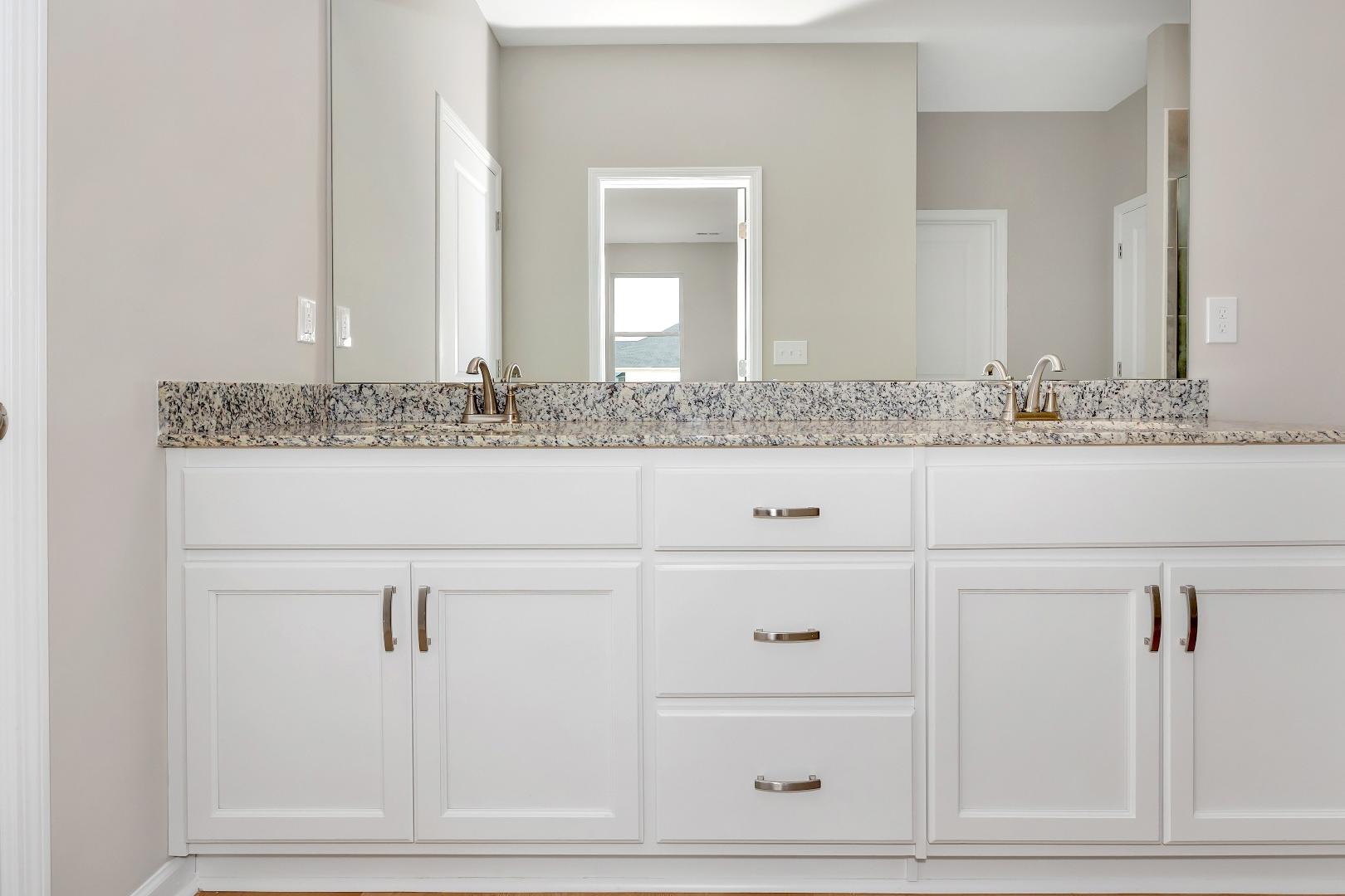 Master bathroom double vanity in The Orion home with white shaker cabinets, granite countertop, and dual sinks