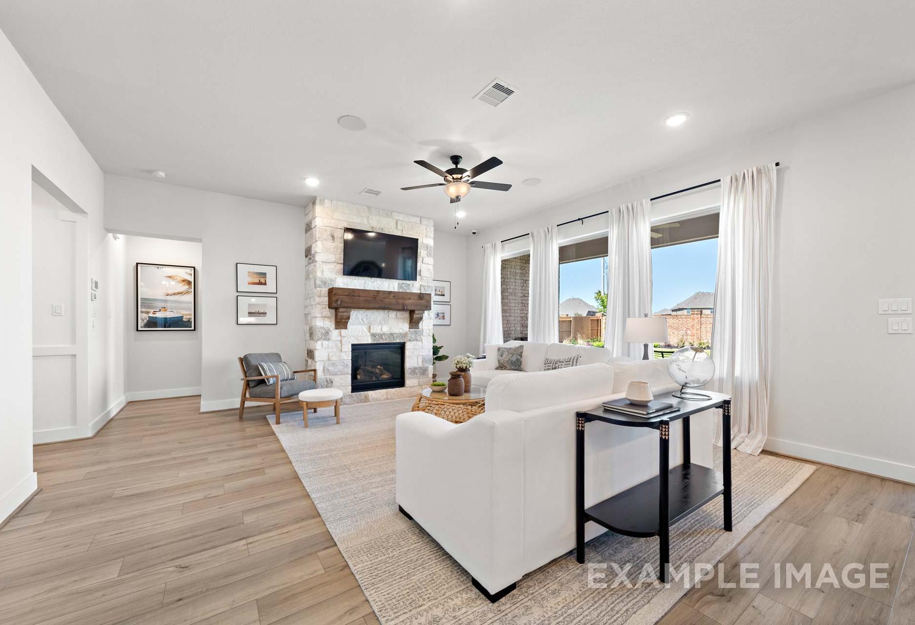 Spacious living room in The Edward A featuring stone fireplace with mounted TV, white sectional sofa, large windows, hardwood floors