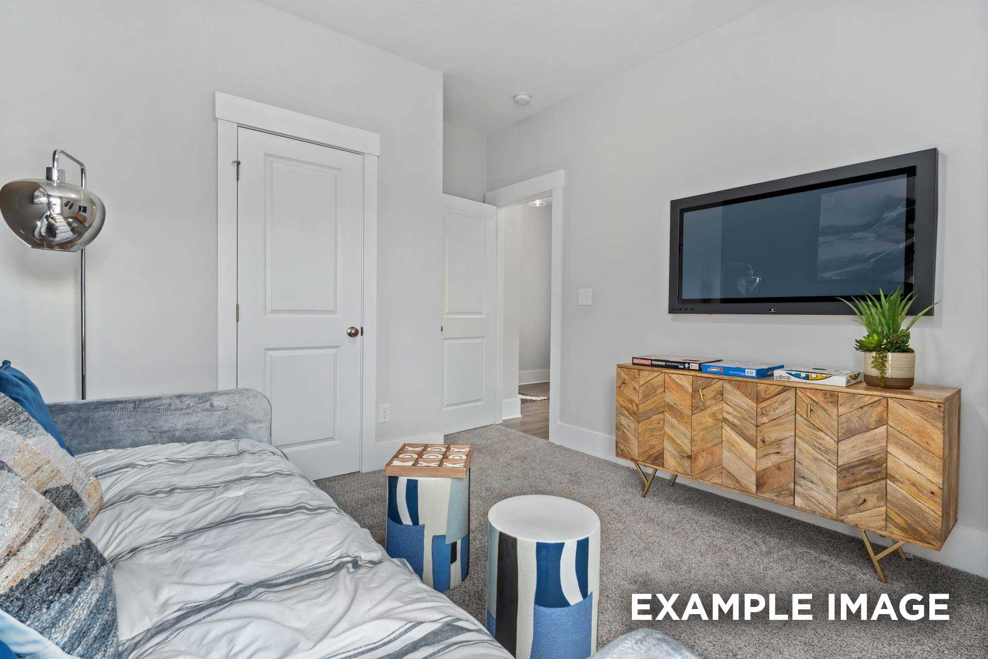 Cozy living room in The Franklin C home design featuring gray velvet sofa, wall-mounted TV, wooden media console with plants, and modern side tables