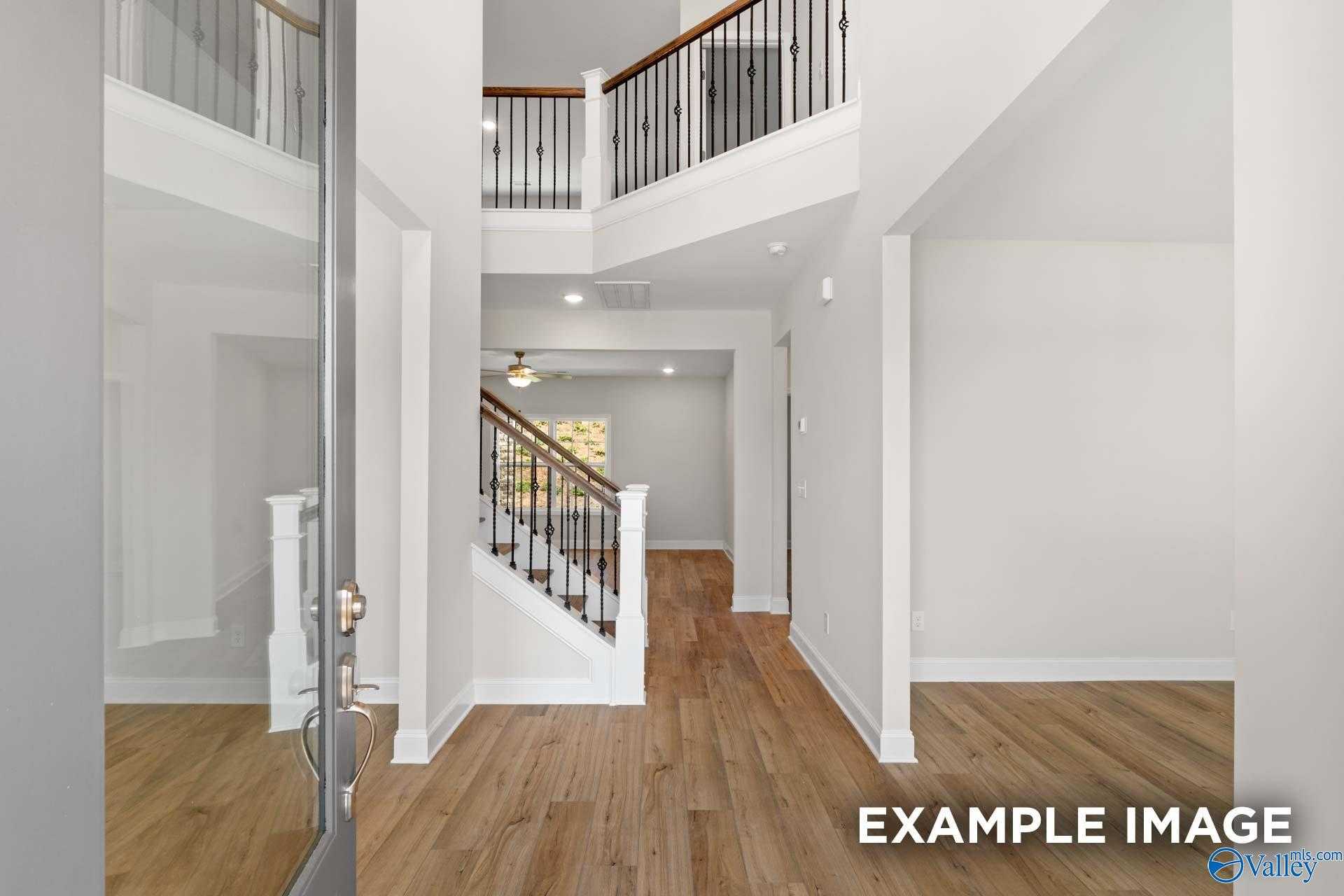Grand two-story foyer with sweeping wooden staircase, black iron balcony, and hardwood floors in Davidson Homes The Madison A, Meridianville