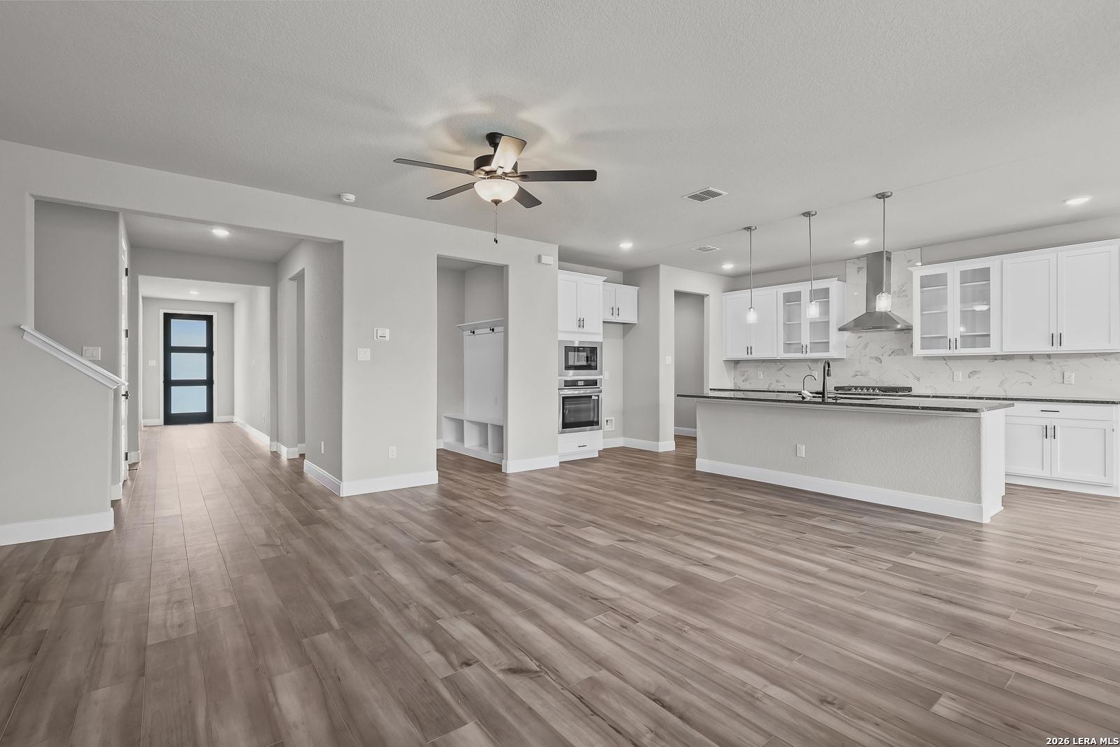 Open-concept kitchen with white shaker cabinets, stainless steel appliances, granite island, and adjacent hallway in Davidson Homes The Belmont H, Castroville, Texas