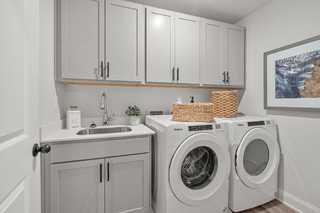 Modern laundry room in The Washington H townhome featuring gray shaker cabinets, utility sink, and white front-load washer dryer
