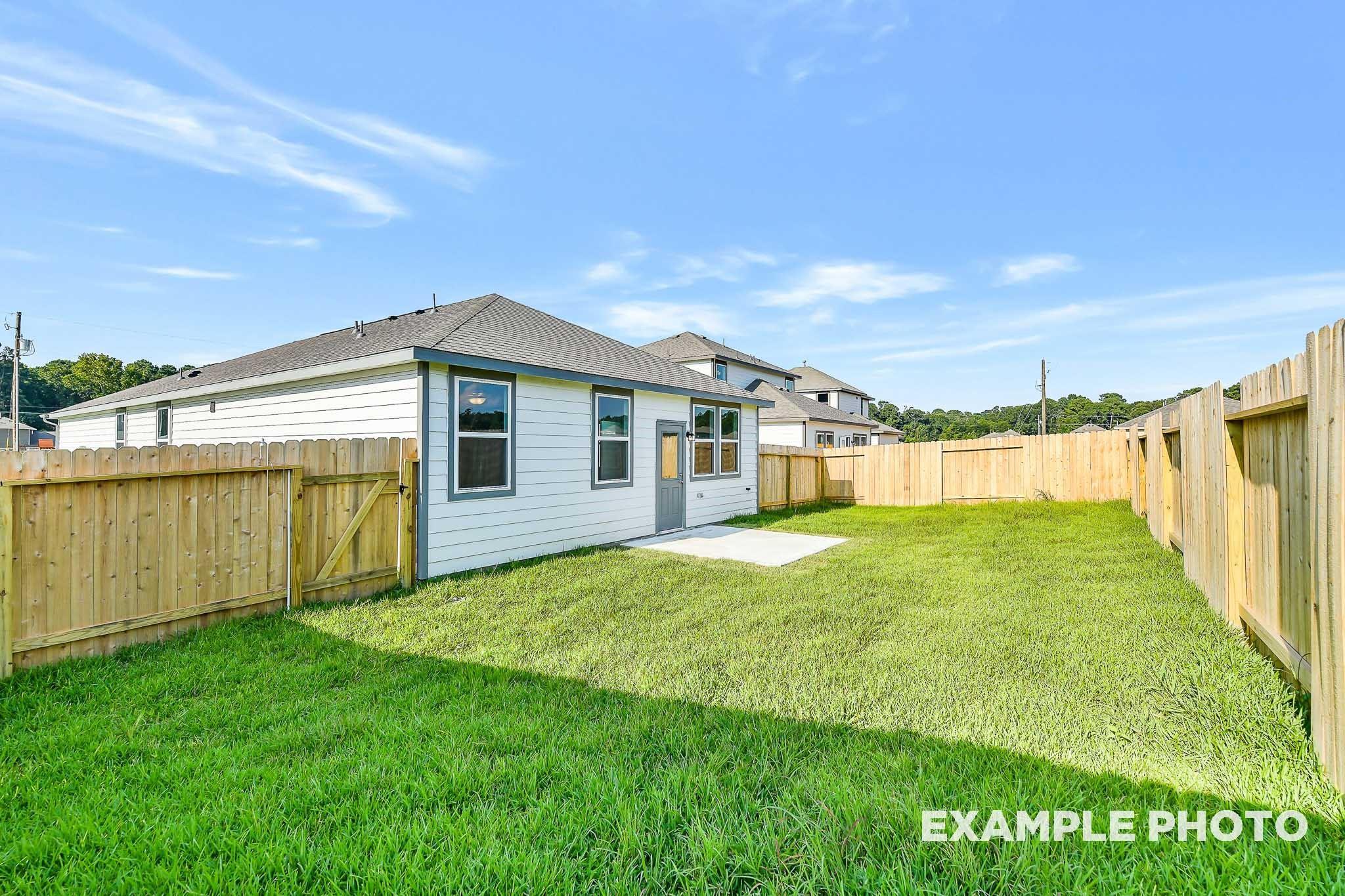 Spacious fenced backyard with lush green lawn beside white single-story home, The Colorado G by Davidson Homes in Conroe, Texas