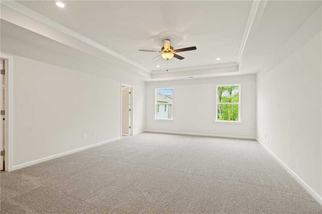 Spacious empty bedroom with tray ceiling, ceiling fan, and large windows in Davidson Homes The Cary B, Kennesaw, Georgia