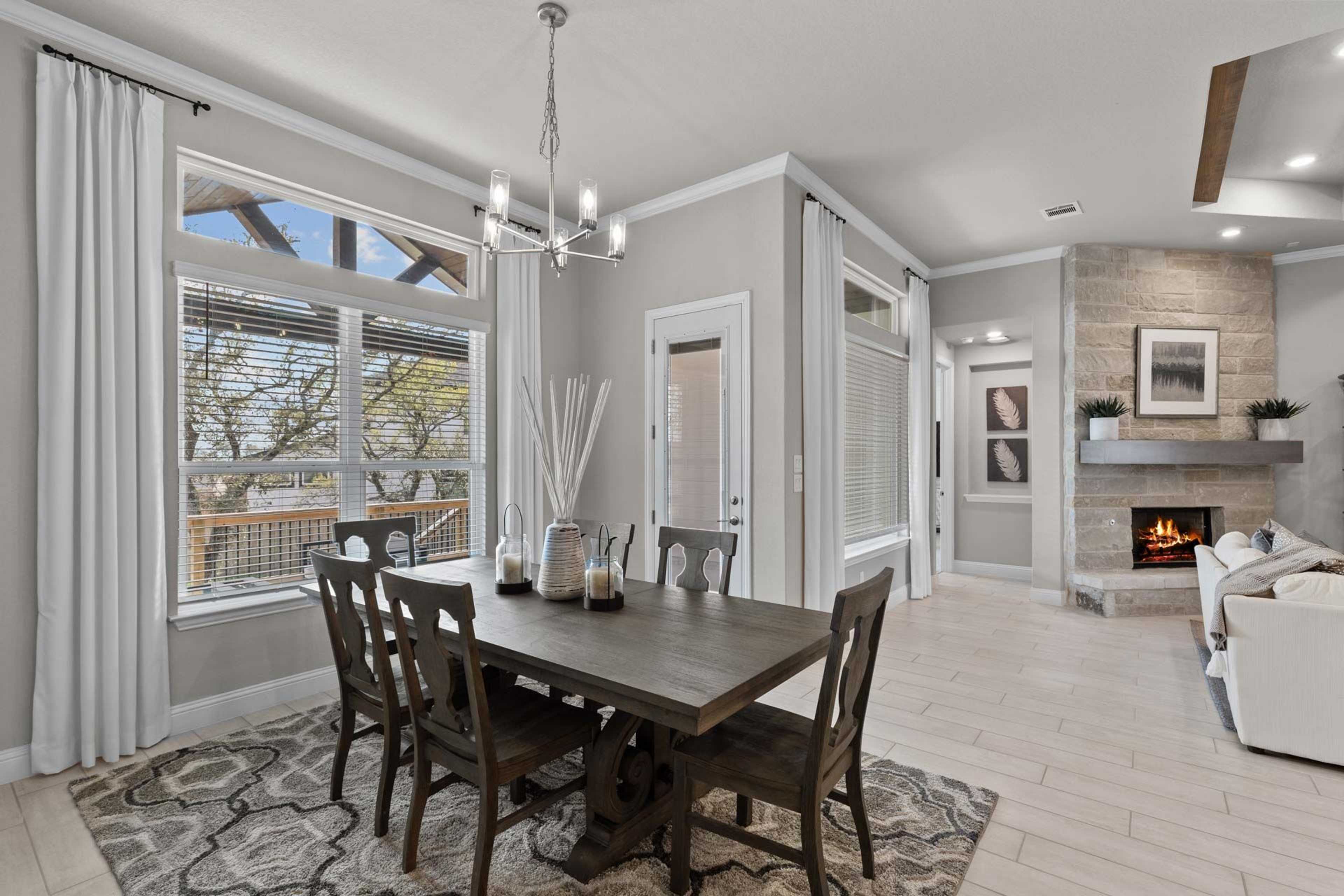 Spacious dining room with farmhouse table, chandelier, and large windows in Ladera San Antonio home by Davidson Homes, open to living area with stone fireplace