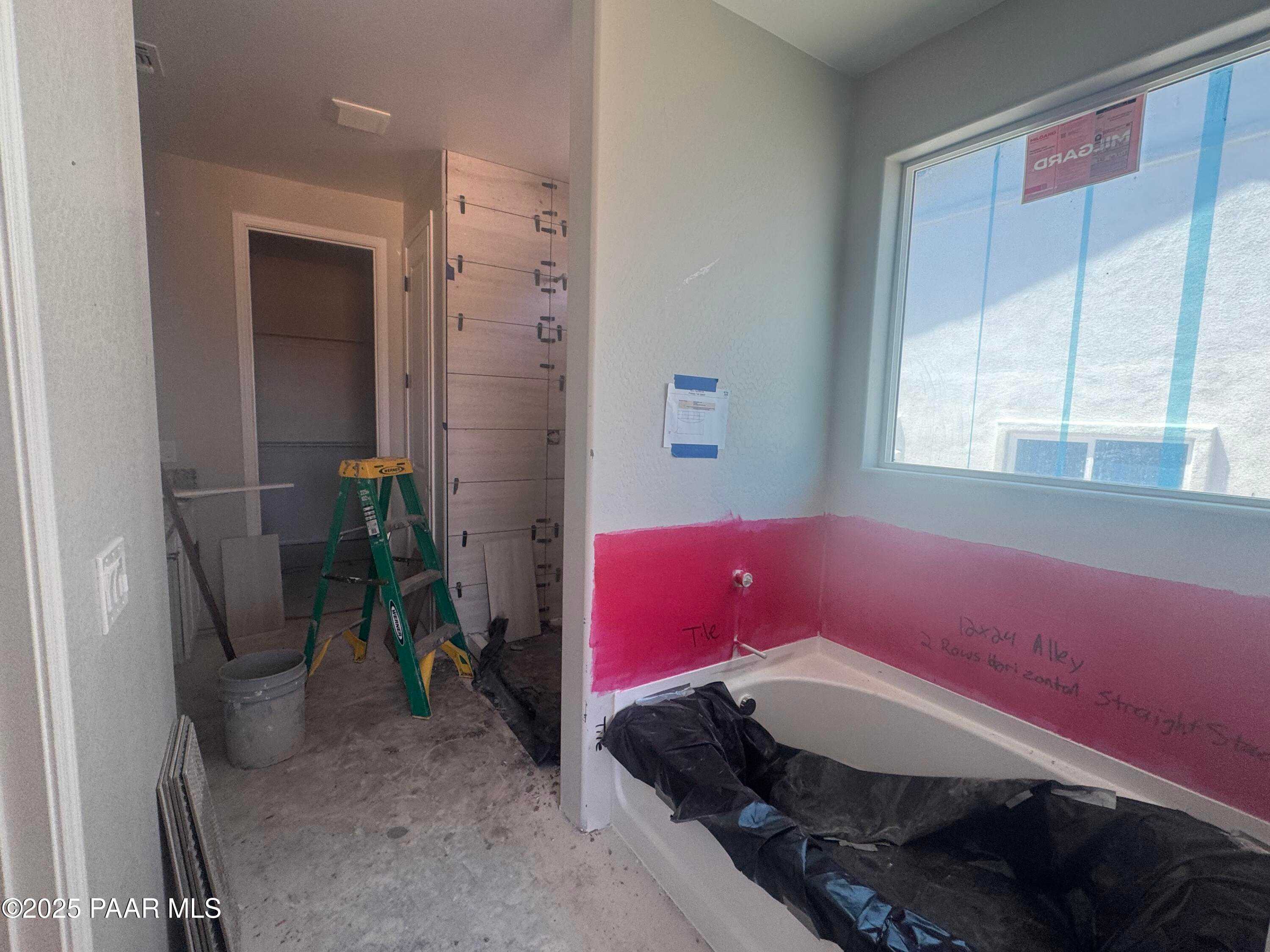 Under-construction bathroom with pink insulated wall, covered bathtub, ladder, and large window in The Daybreak E home, Prescott, AZ