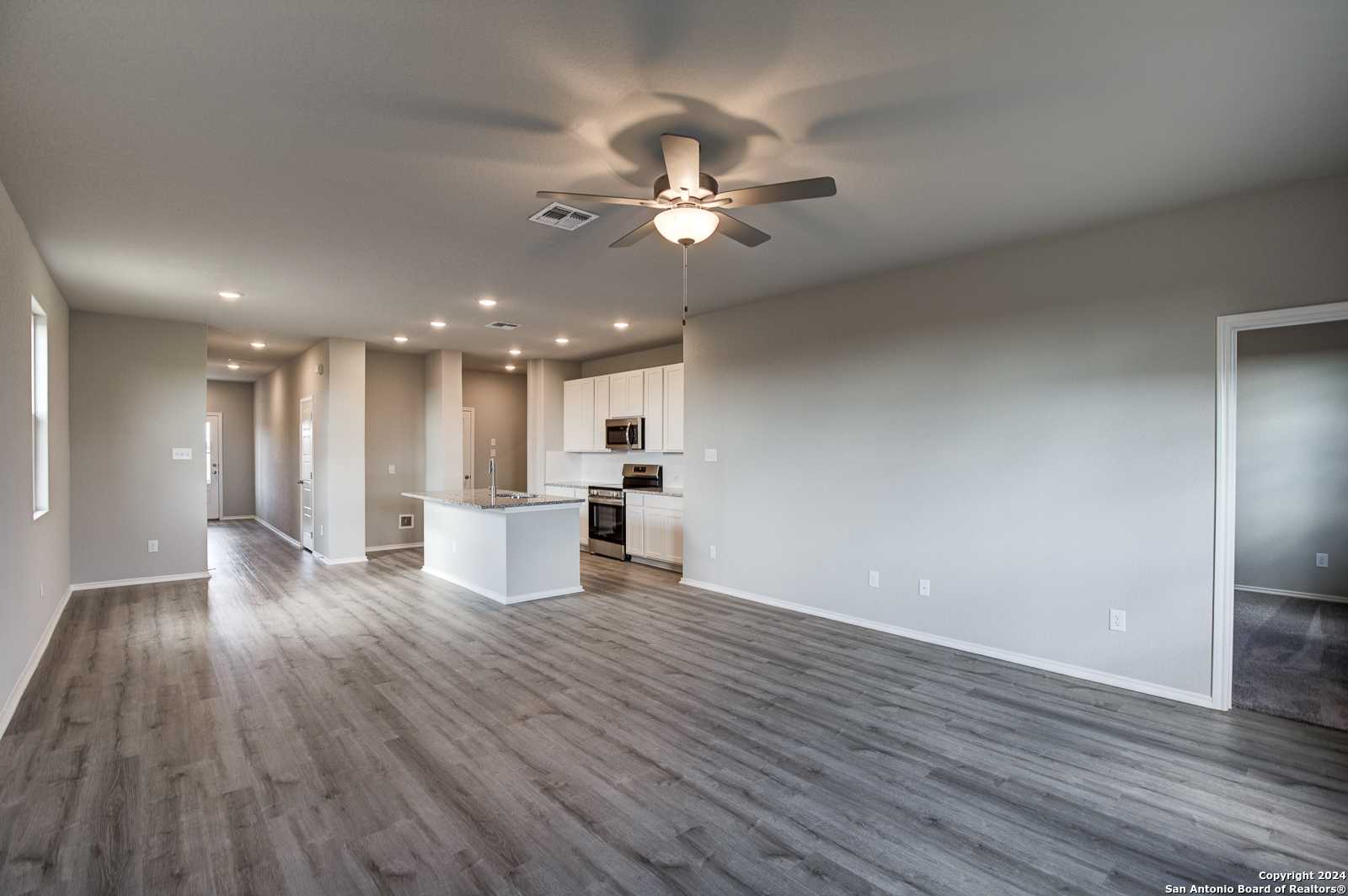 Open-concept kitchen-living area with white cabinets, island, ceiling fans, and laminate floors in Davidson Homes The Blanco C, San Antonio