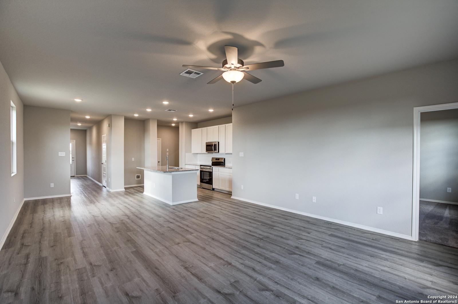 Open-concept kitchen-living area with white cabinets, island, stainless appliances, and ceiling fans in Davidson Homes The Blanco C, San Antonio