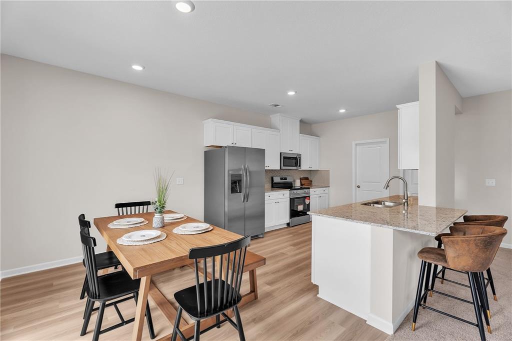 Open-concept kitchen with white cabinets, stainless appliances, granite island, and adjacent wooden dining table in Davidson Homes The Bartlett, Phenix City, Alabama