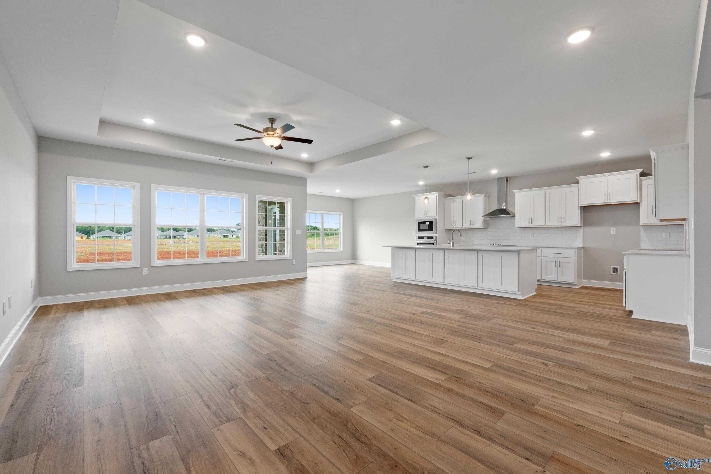Open-concept kitchen and living space with white cabinets, large windows, island, ceiling fan, and hardwood floors in Davidson Homes The Finleigh, Meridianville AL