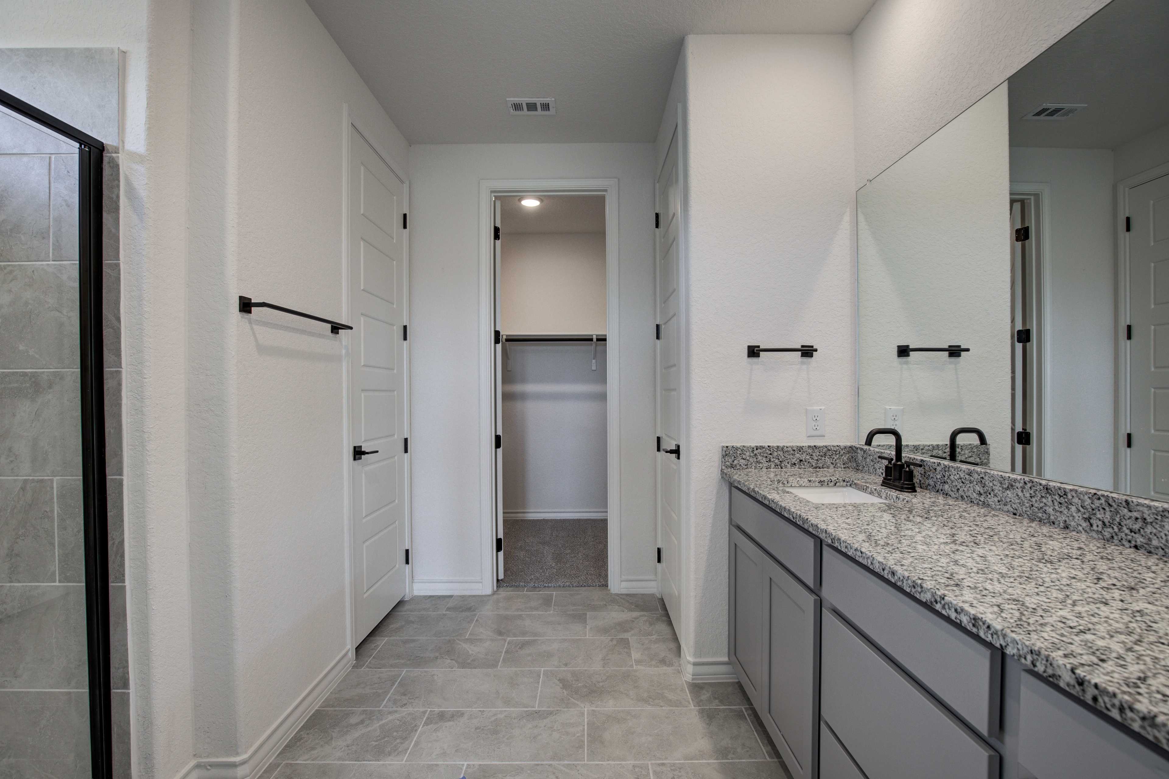 Spacious master bathroom in The Lanier with double vanity, granite counters, glass walk-in shower, and adjacent closet