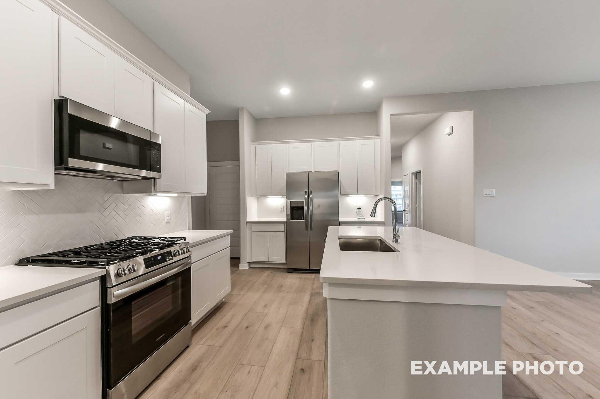Spacious modern kitchen in The Laguna B featuring white shaker cabinets, large quartz island with sink, stainless steel gas range and appliances