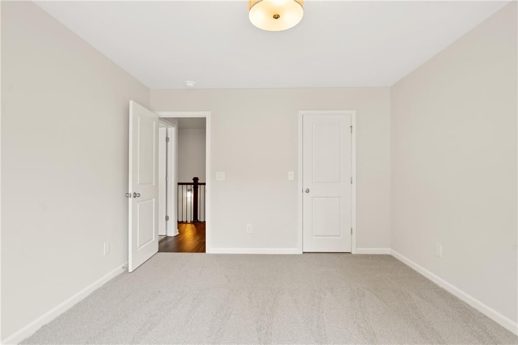 Spacious empty bedroom with neutral beige walls, light carpet, and open door to wooden staircase in Davidson Homes The Cary B, Kennesaw, Georgia