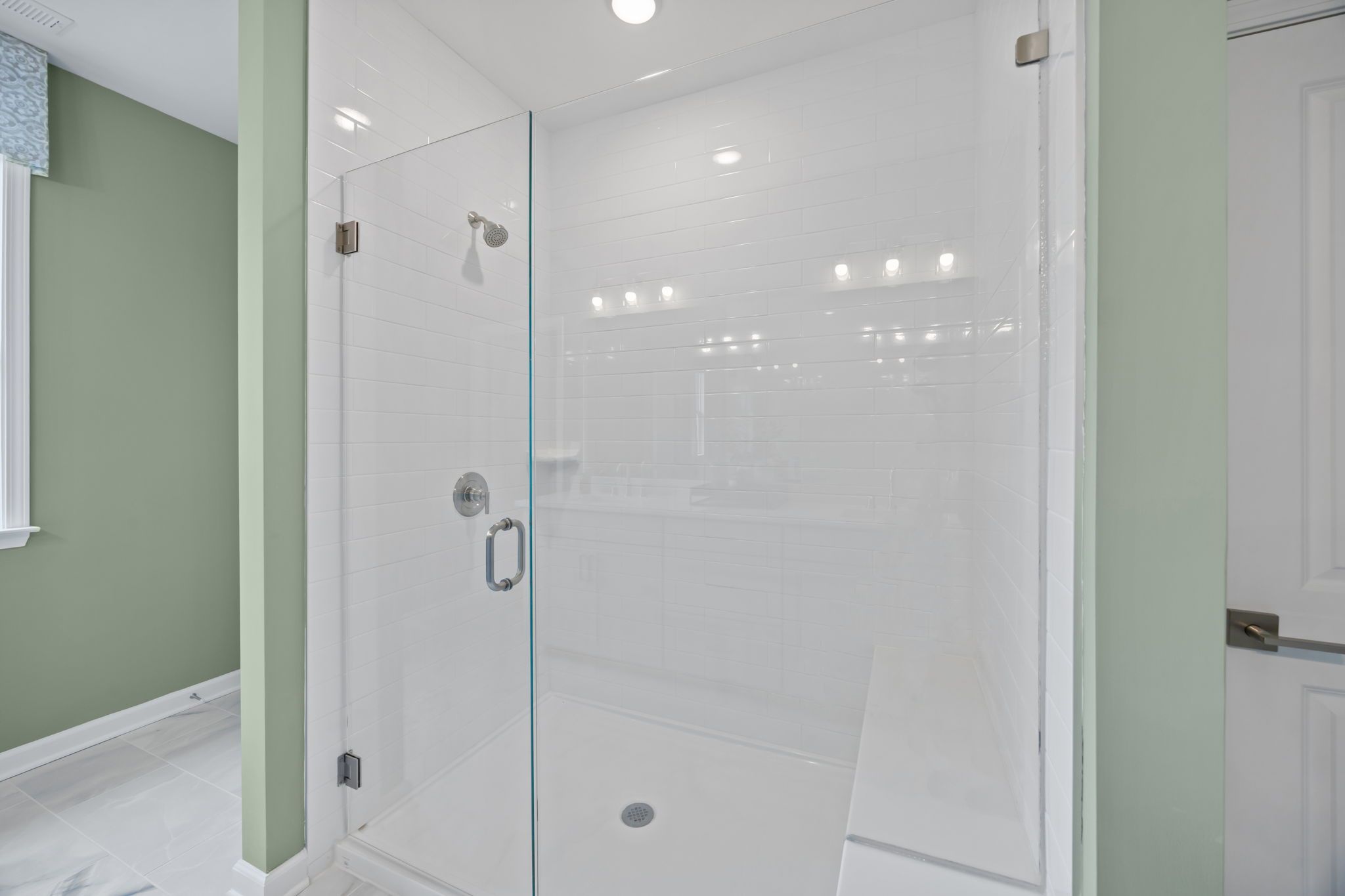 Walk-in shower with white subway tile, glass door, and built-in bench at Springvale South in Fuquay-Varina by Davidson Homes.