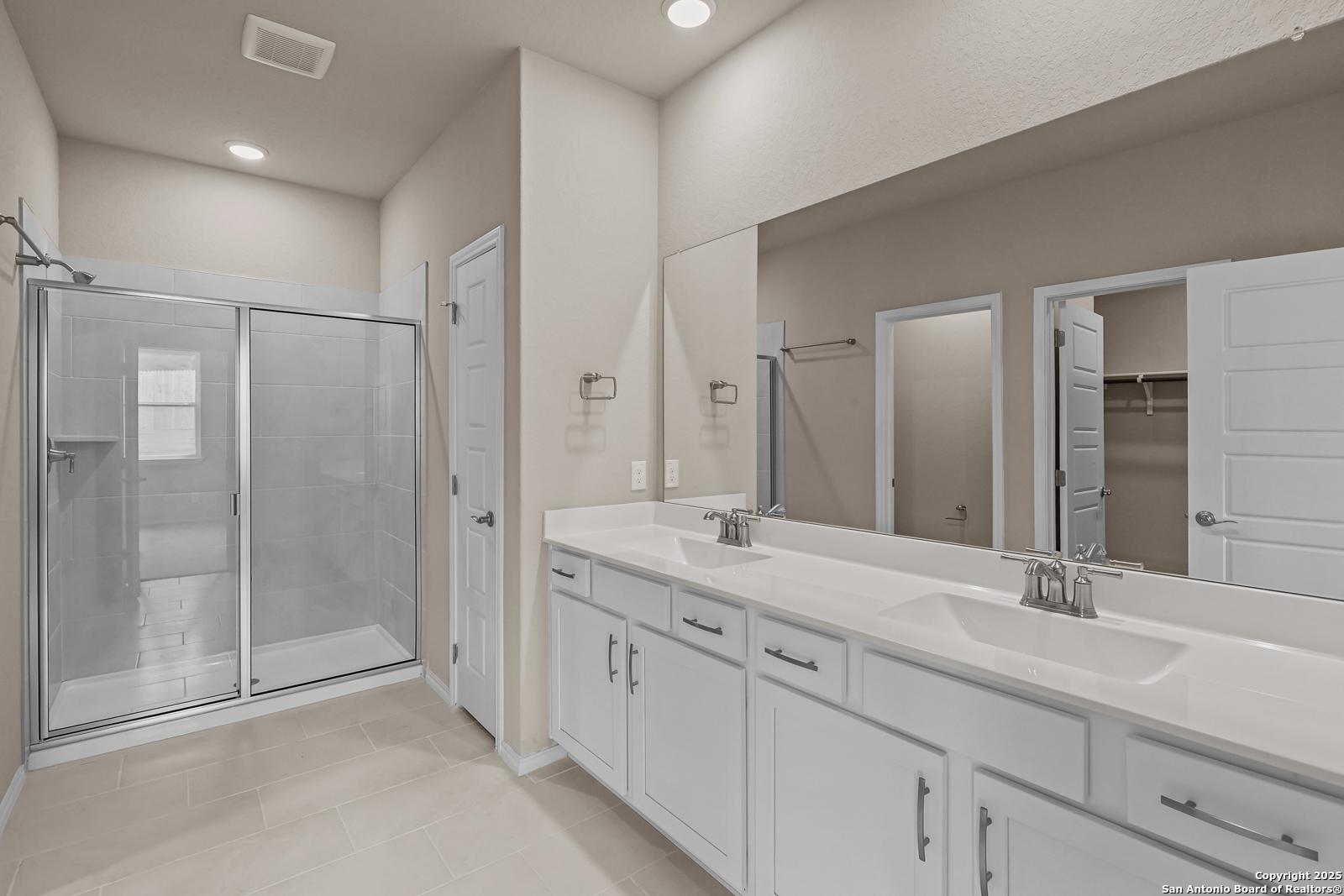 Modern master bathroom with double vanity, frameless glass shower, and linen closet in Davidson Homes The Douglas G, San Antonio, Texas