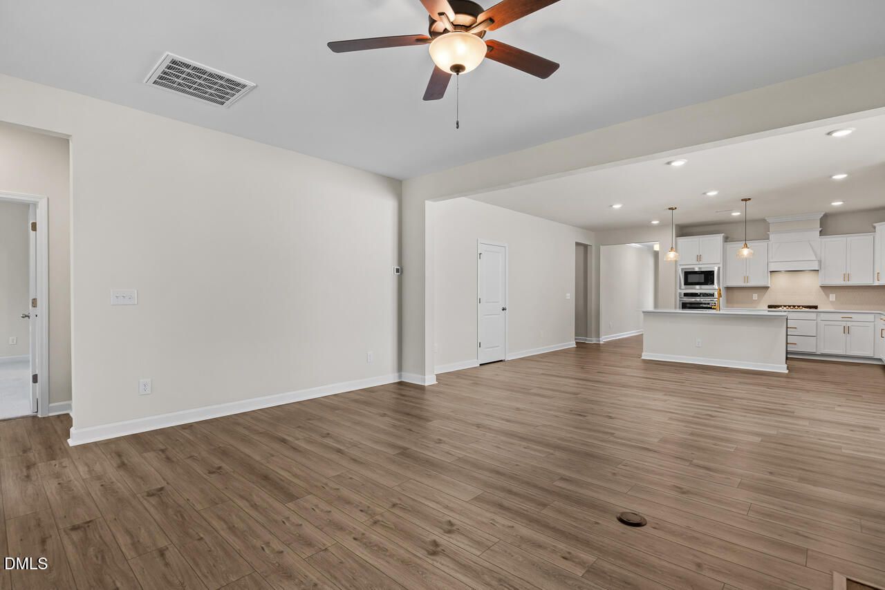 Open-concept living room with wood-look flooring and ceiling fan flowing into white kitchen in The Birch II C, Wake Forest home
