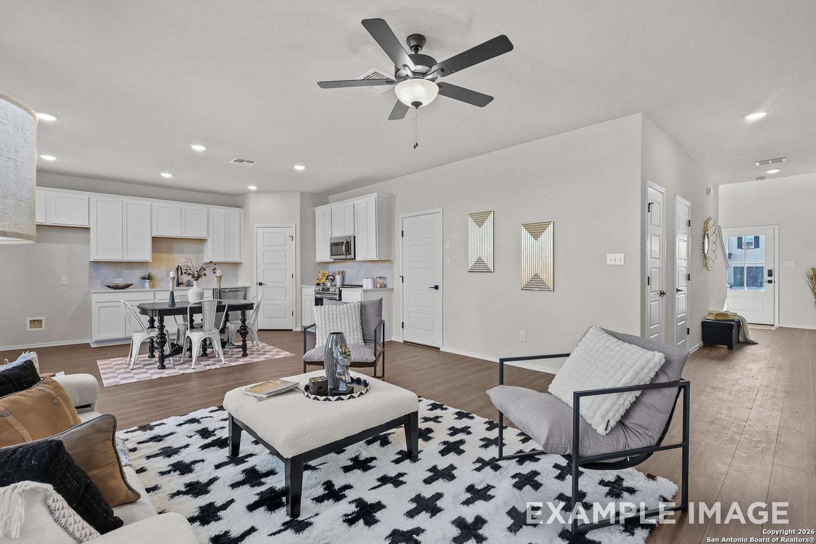 Modern open-concept living and dining area with white kitchen cabinets, ceiling fan, and patterned rug in Davidson Homes The Trinity B, San Antonio