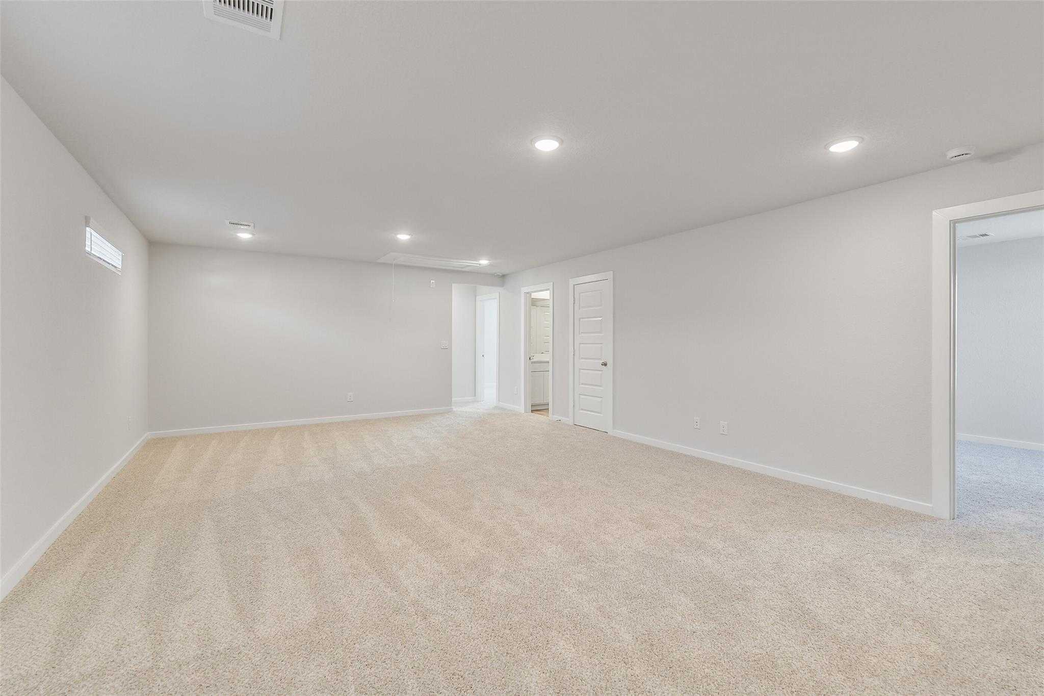 Spacious empty room with beige carpet, white walls, recessed lights, and bathroom door in Davidson Homes The Rio Grande H, Magnolia, Texas