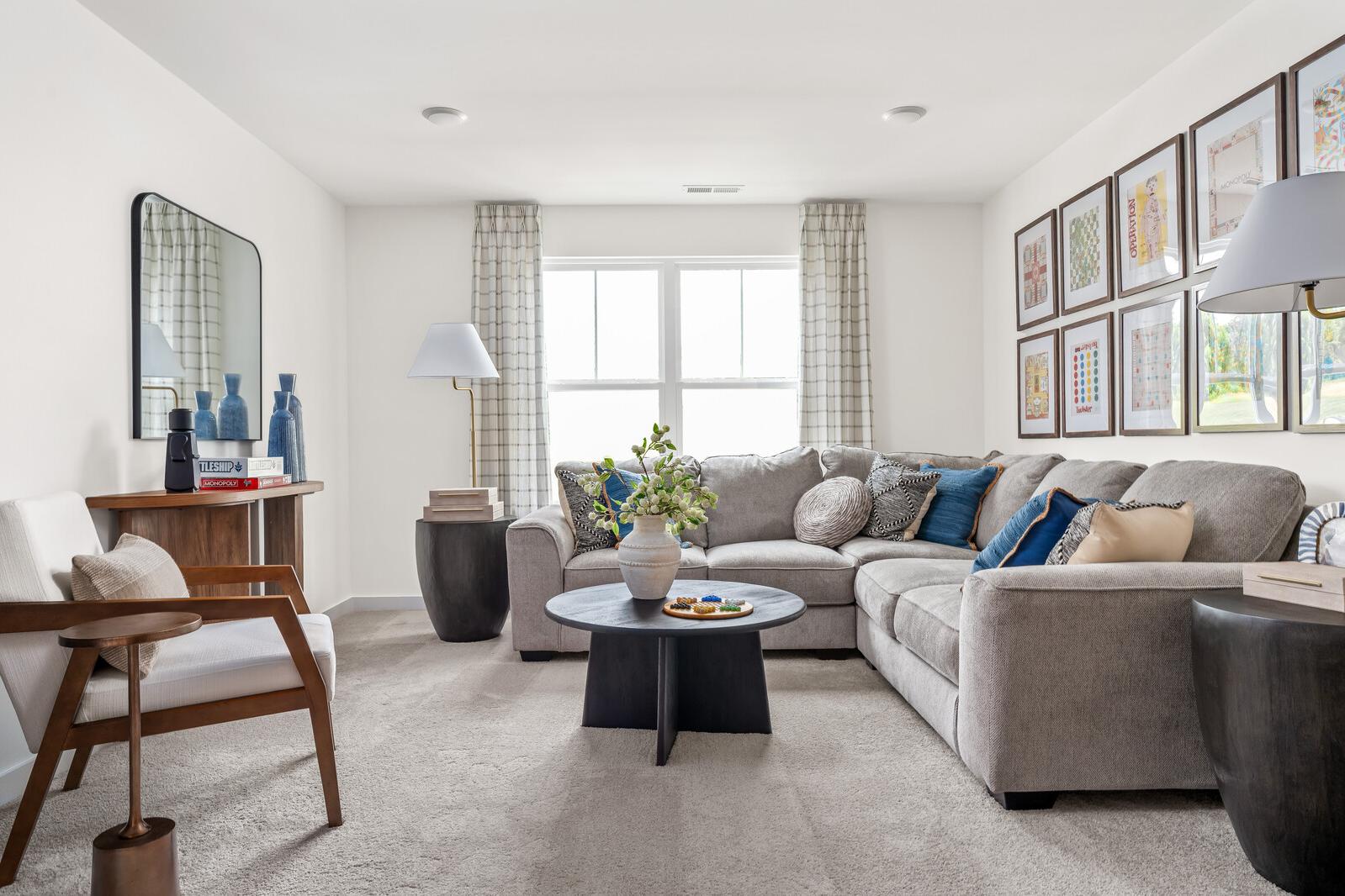 Spacious living room at Woods Crossing in Gallatin TN with gray sectional sofa, wooden tables, and large curtained windows
