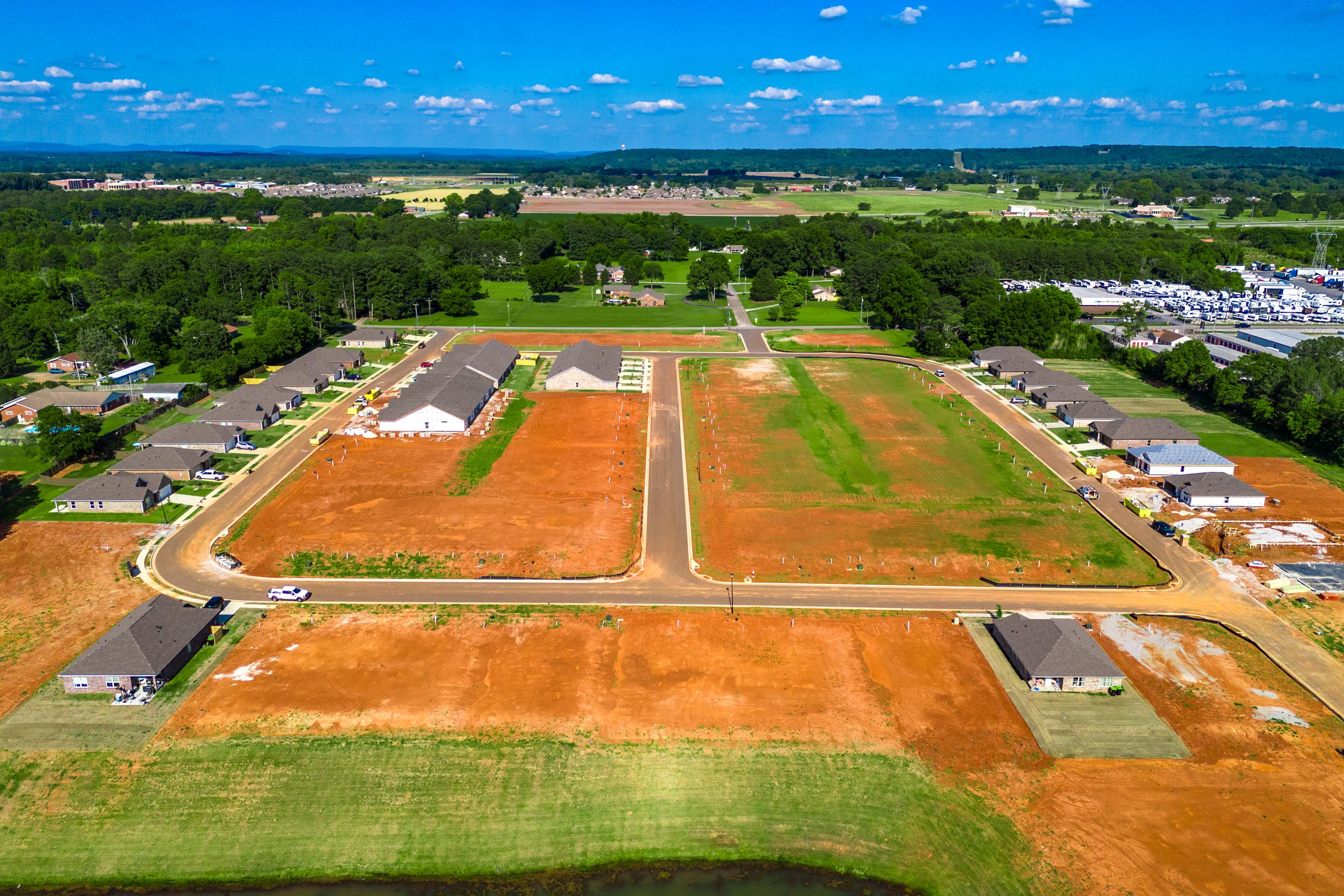 Aerial view of Hollon Meadow in Decatur Alabama featuring new homes, red dirt construction lots, tree-lined streets, and scenic pond by Davidson Homes